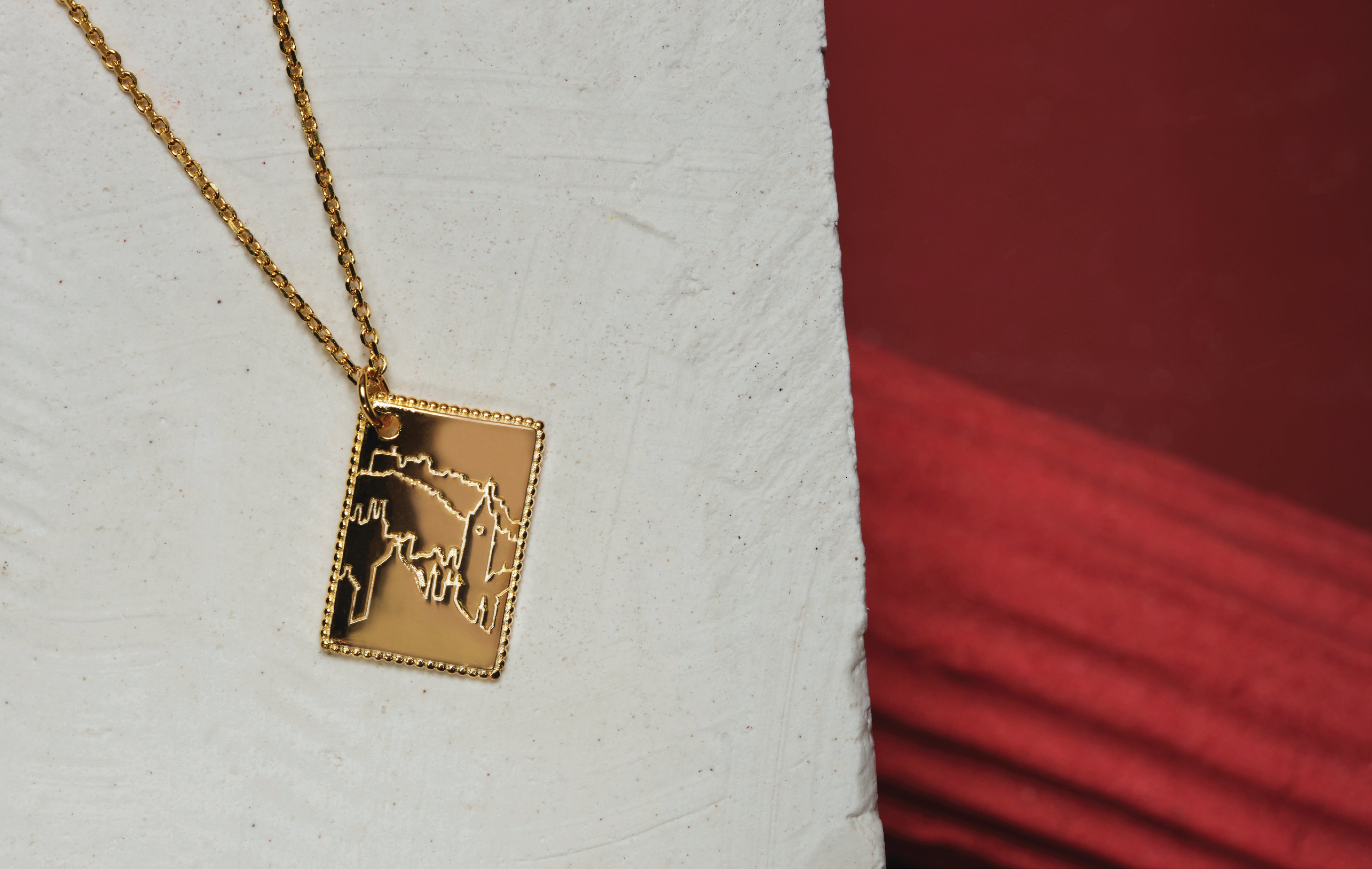 A gold plated necklace. The necklace has a dainty chain and postcard pendant. The pendant has a beautifully detailed engraving of Edinburgh city.