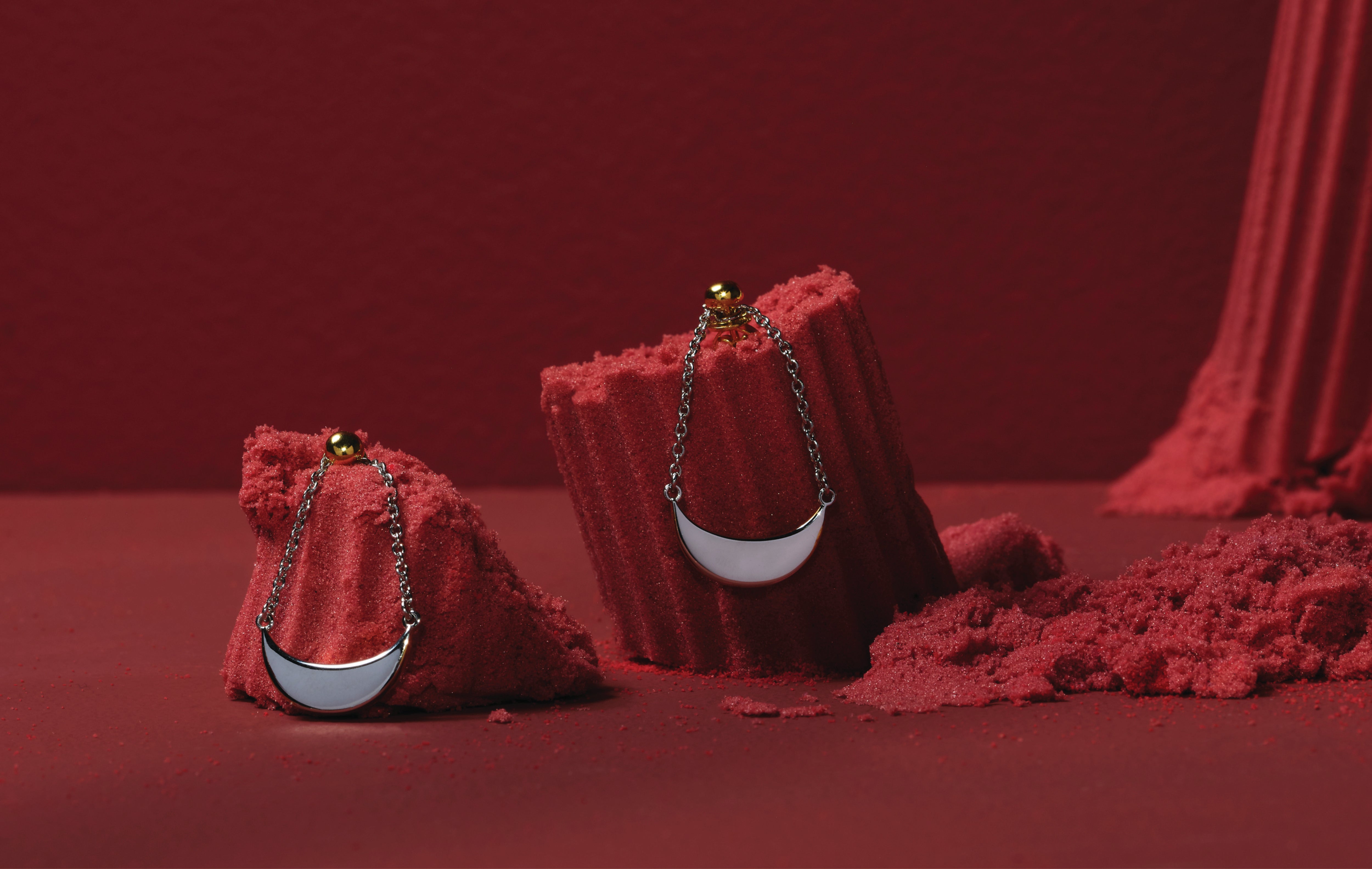 A pair of gold plated earrings. The earrings have 2 dainty chains with a half crescent moon shape hanging horizontally from the chains.