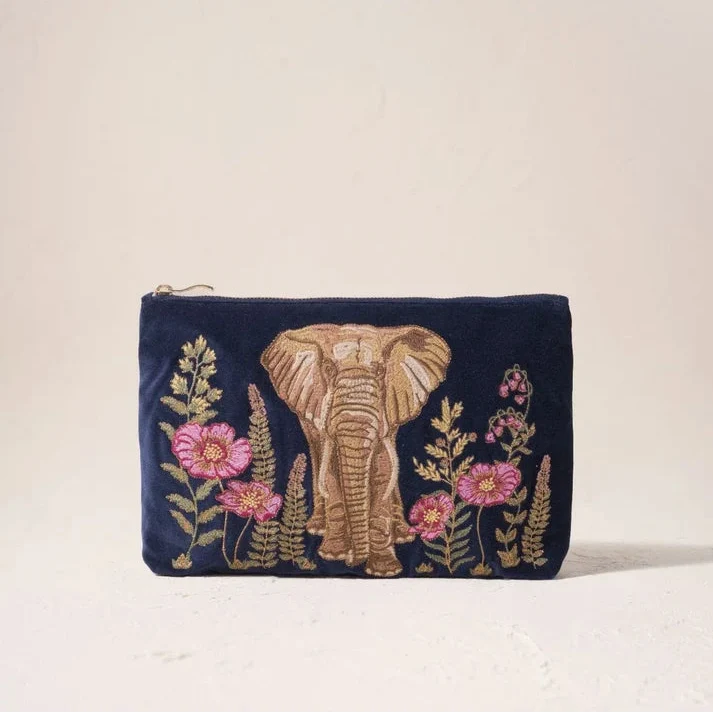 A navy blue velvet zip pouch featuring an embroidered elephant and pink flowers in gold and pink thread, set against a plain beige background.