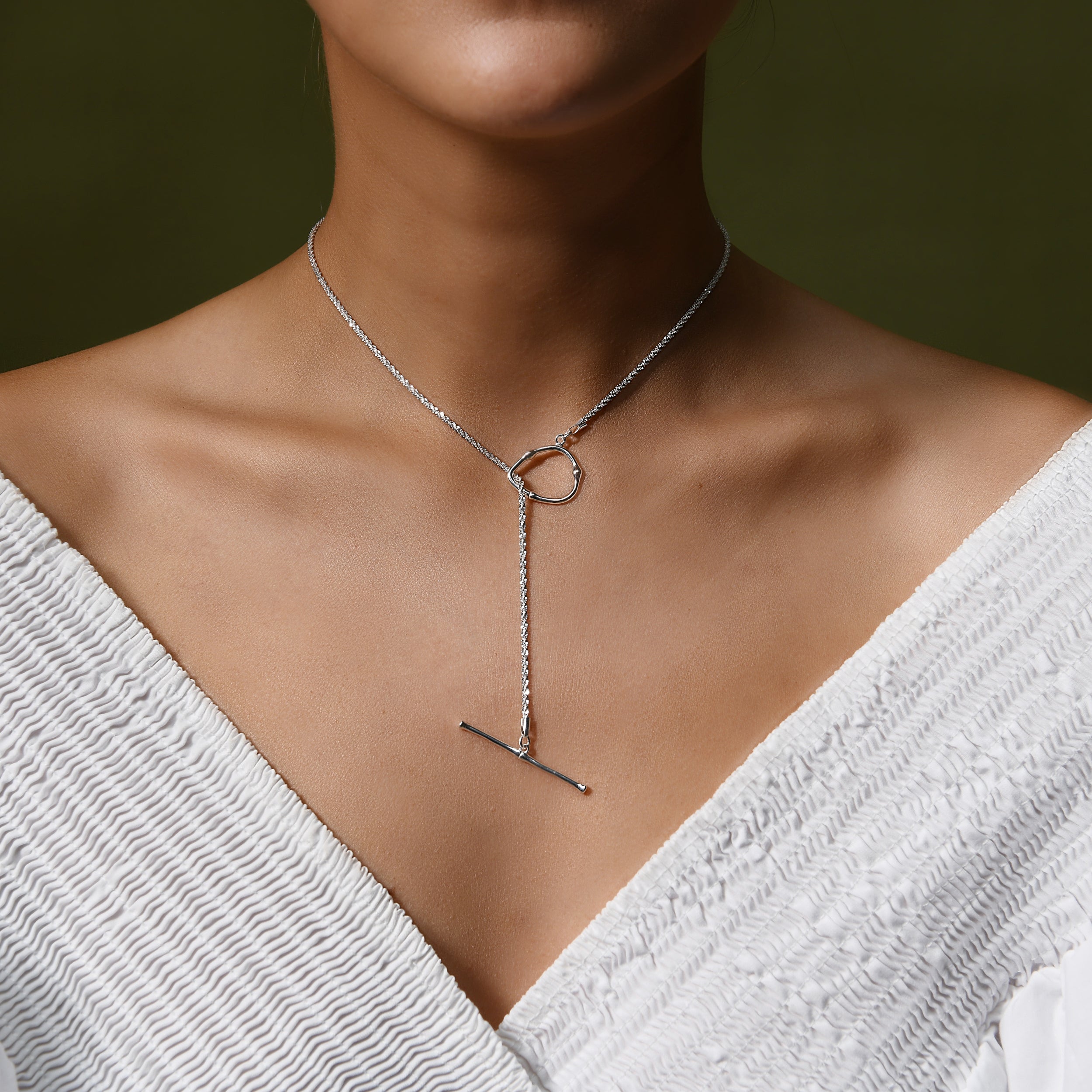 a female model close up photo of the neck wearing a sleek shimmering silver rope chain with a silver toggle