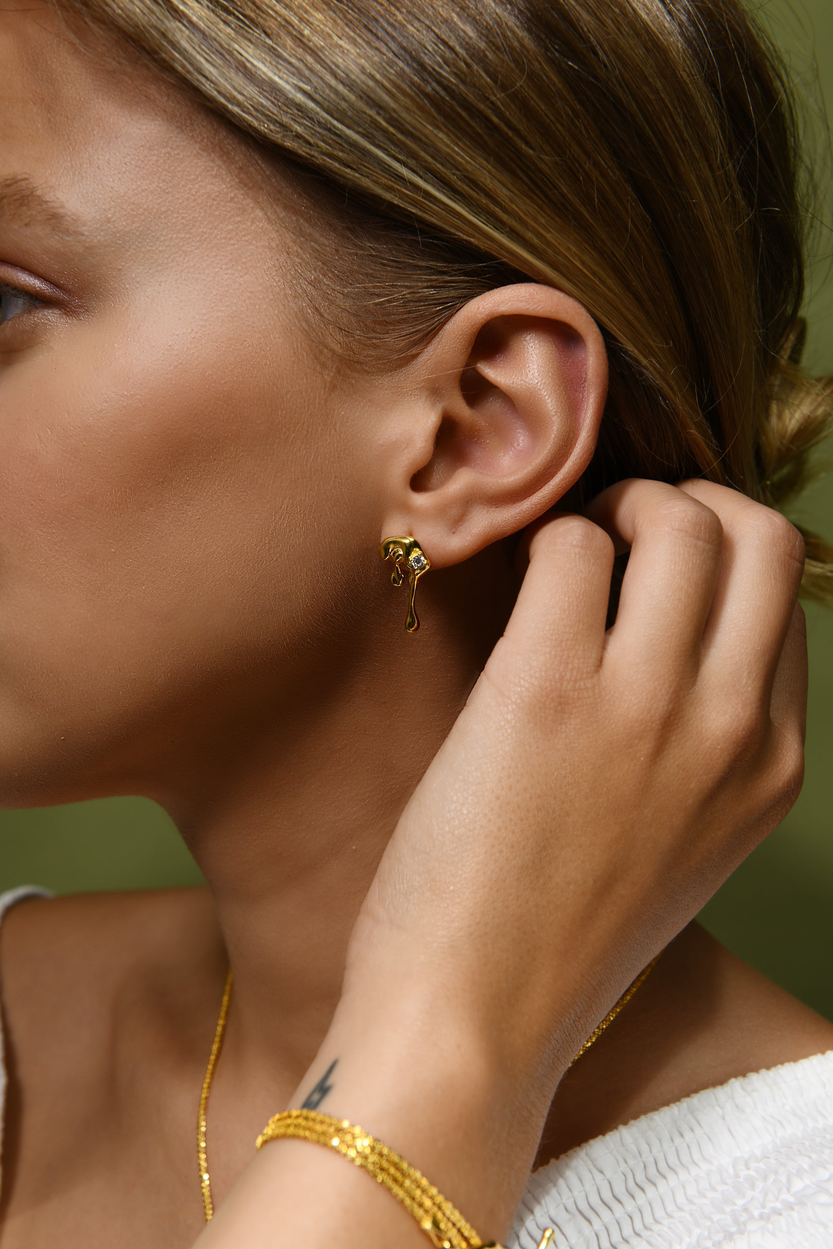 A model wears a pair of gold vermeil stud earrings shaped to resemble water droplets.