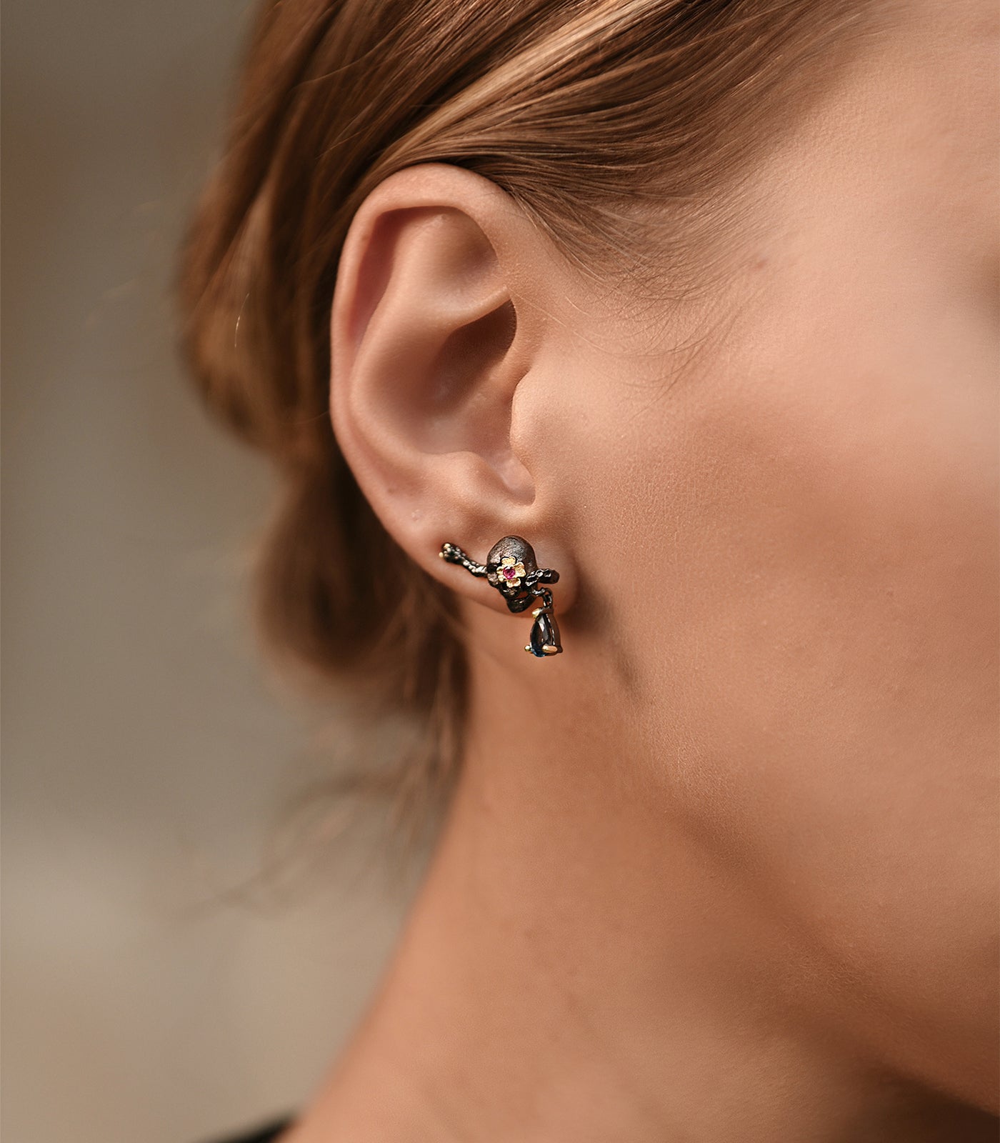 A model wears an oxidised sterling silver skull earring with a gold vermeil flower, pink ruby and blue topaz gemstones.