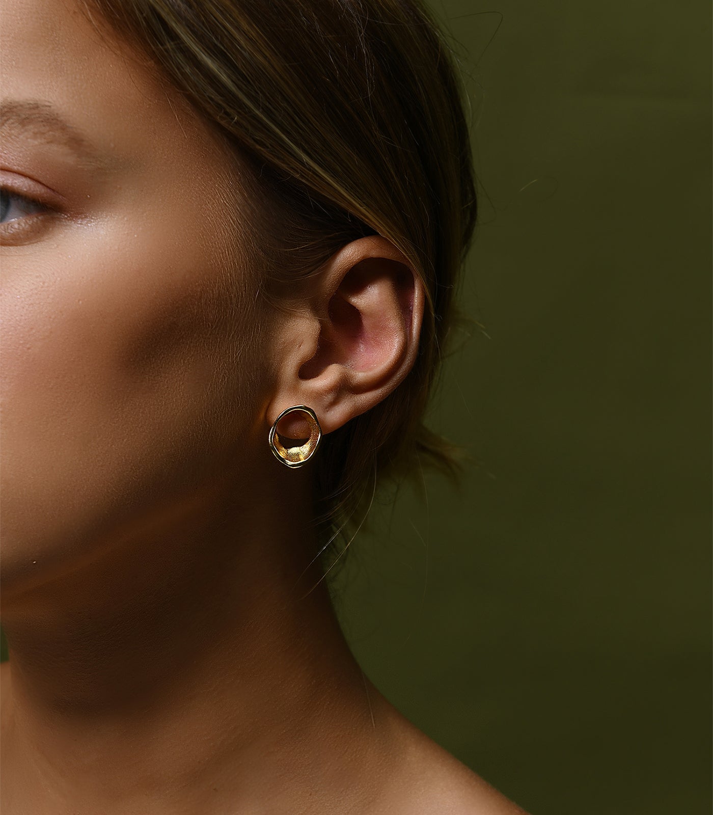 A gold vermeil circle stud earring. The earring has an irregular shape which resembles the movement of water.