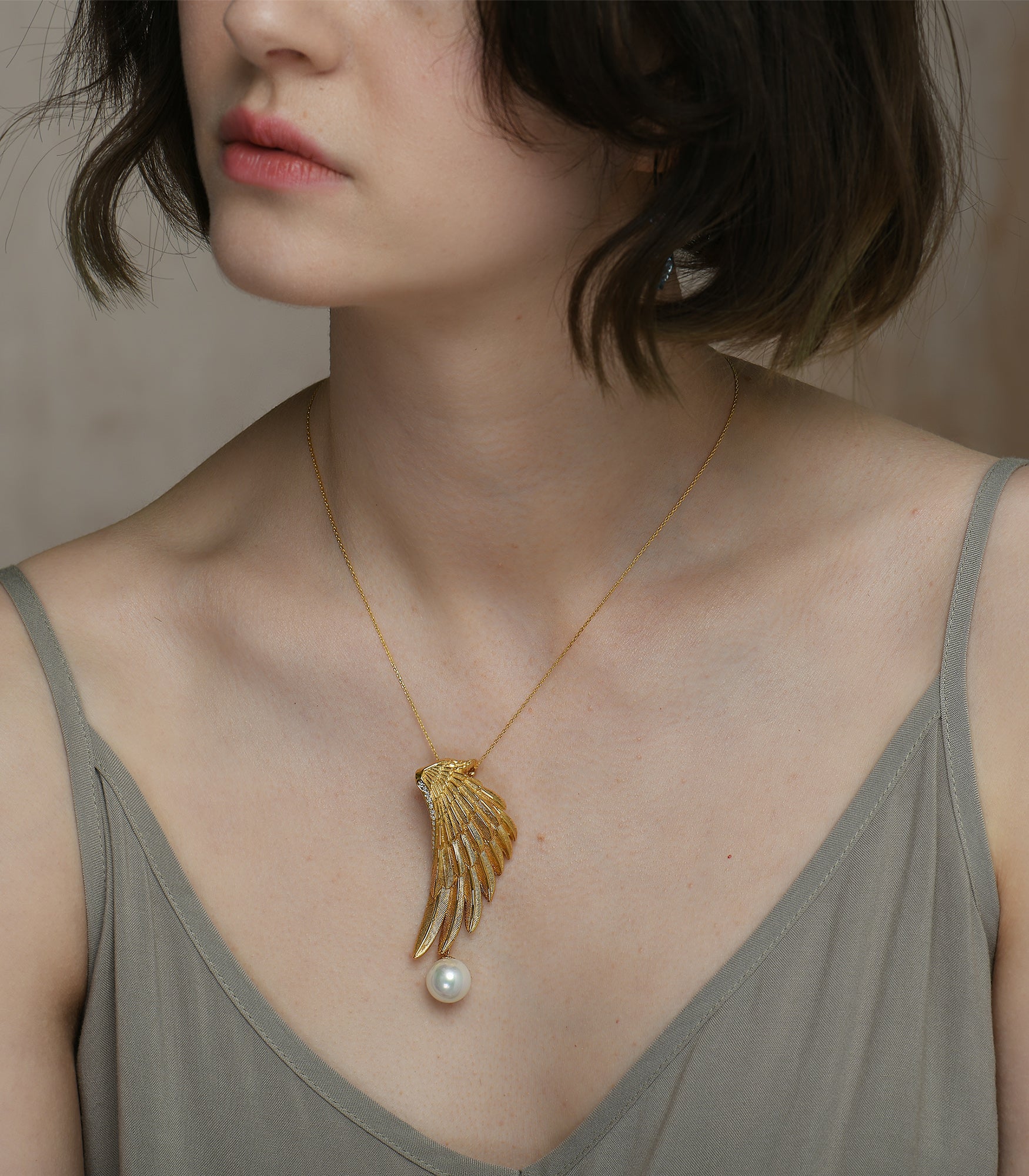 A lady wearing a gold vermeil necklace which has an eagle wing pendant with a white pearl hanging from it.