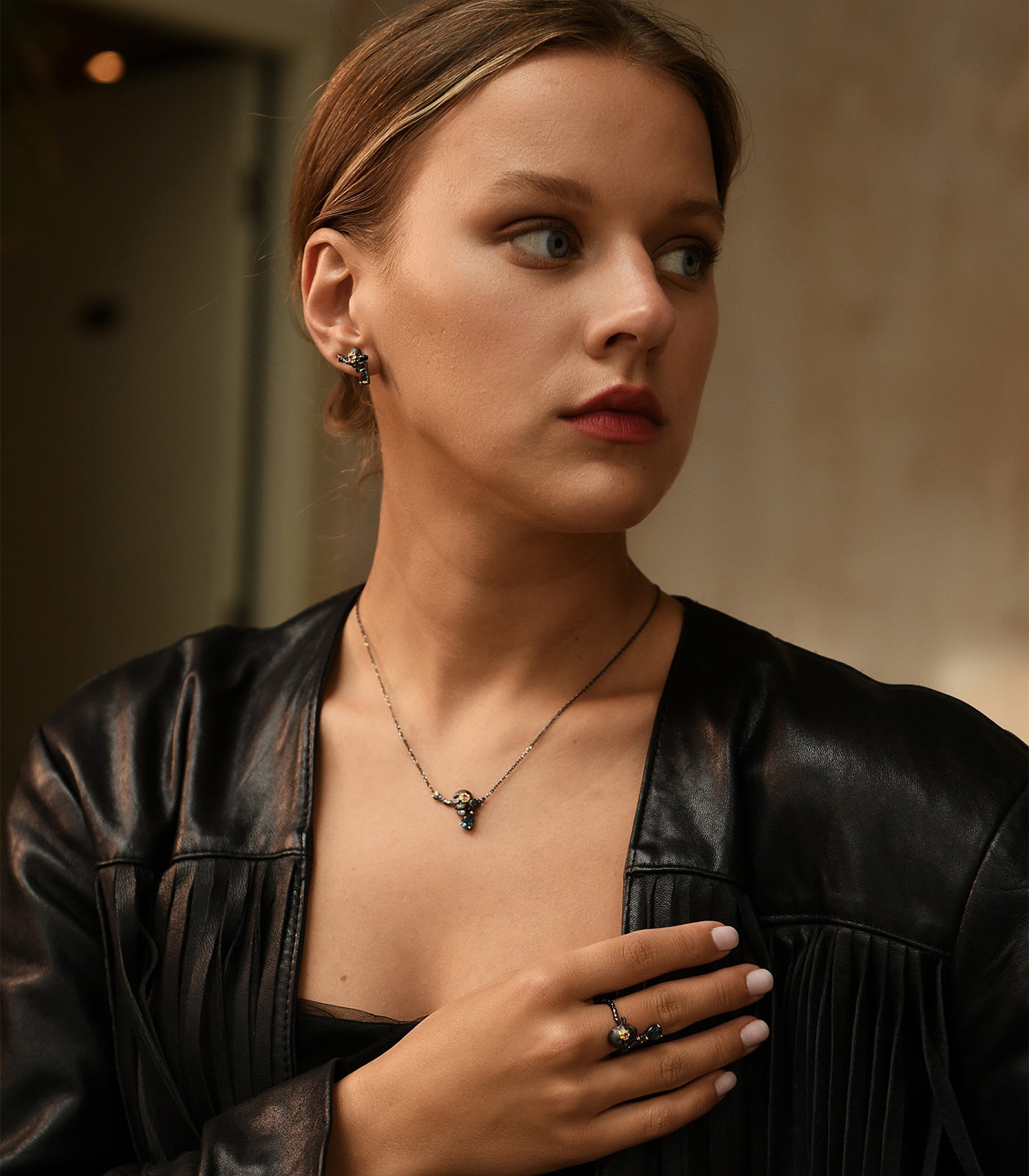 A model wears a completed set of oxidised sterling silver skull jewellery. The set includes a necklace, earrings and the ring.
