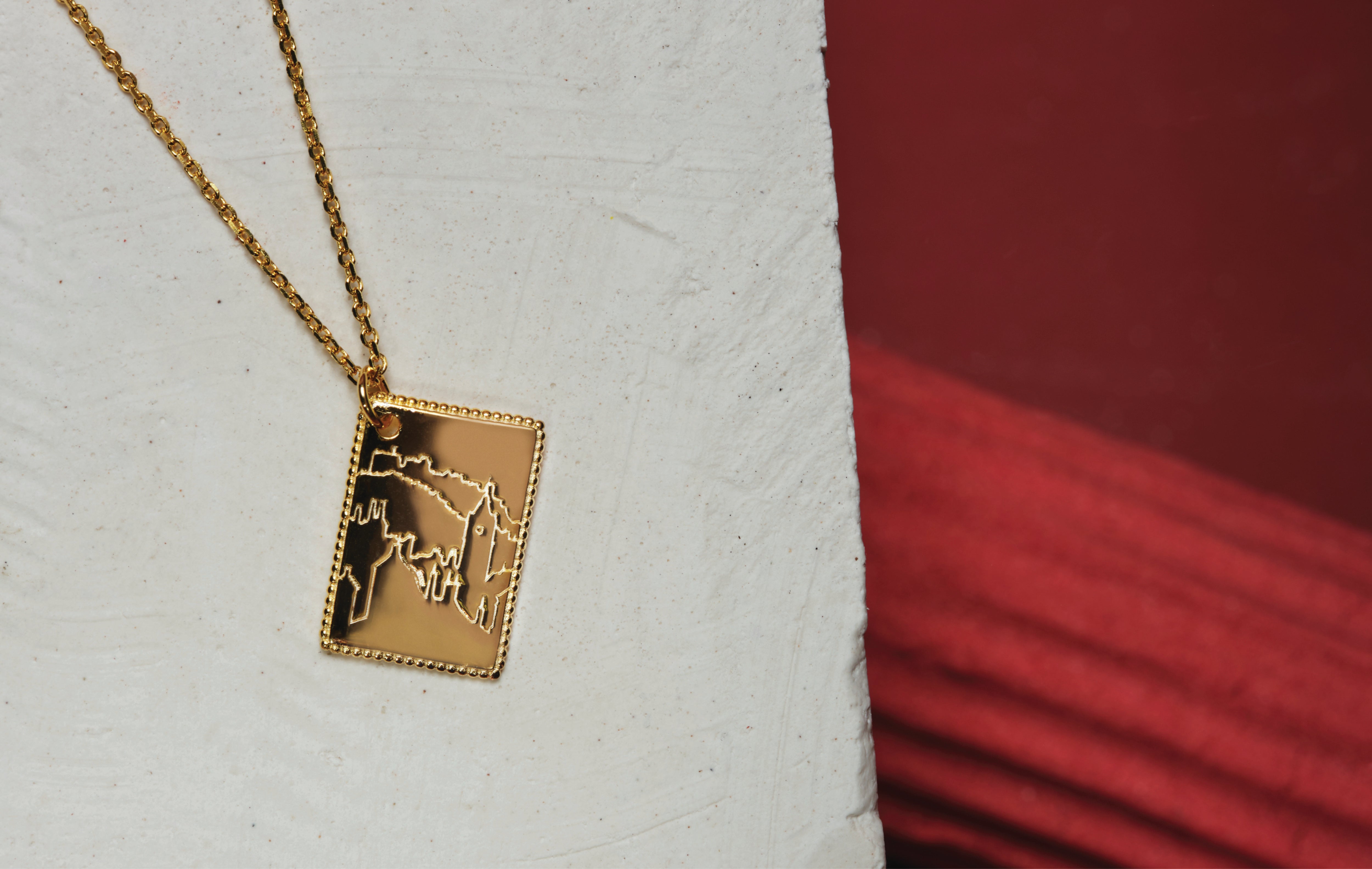 A gold plated necklace. The necklace has a dainty chain and postcard pendant. The pendant has a beautifully detailed engraving of Edinburgh city. 