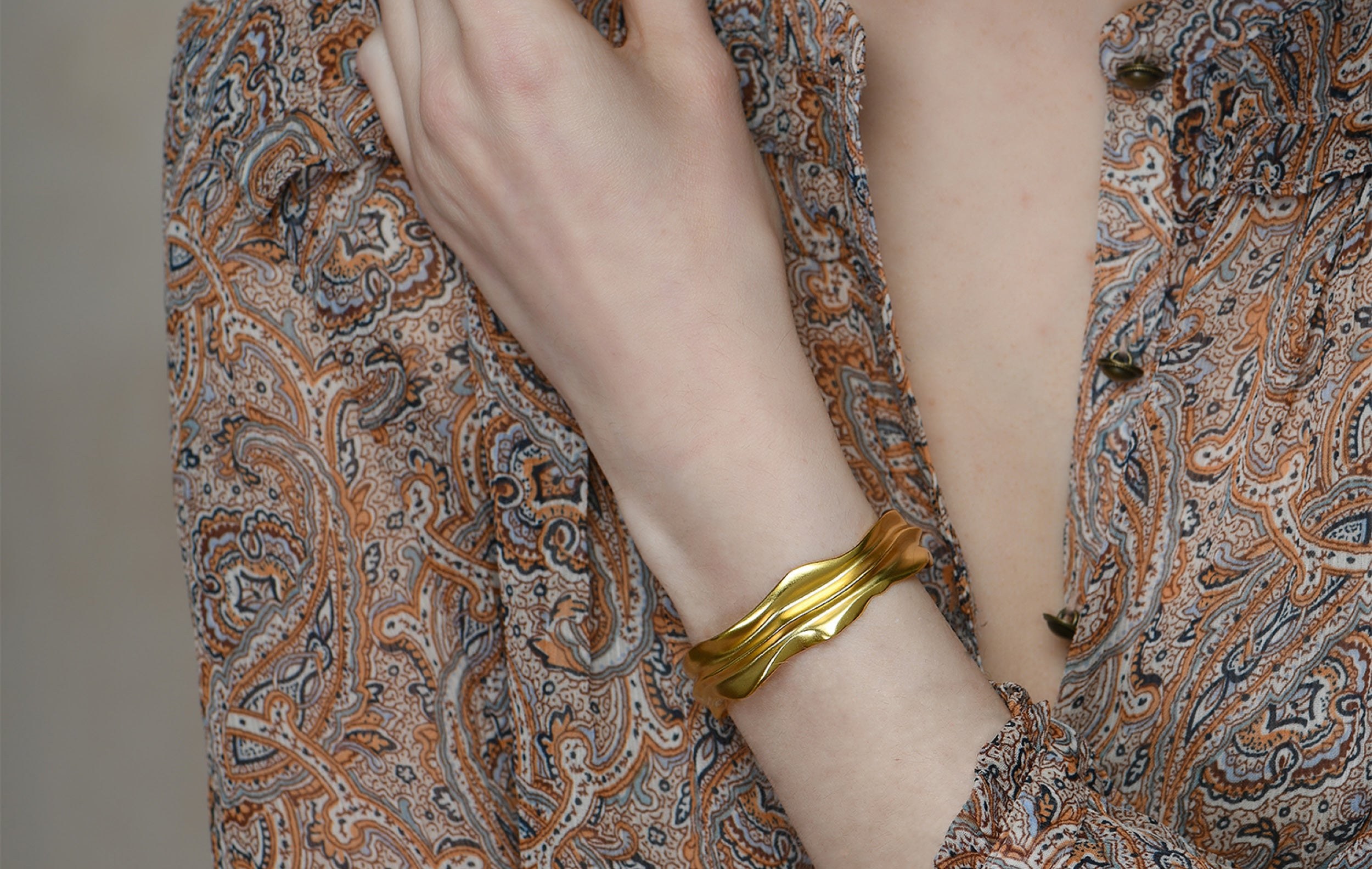 A lady wearing a collection of gold plated sterling silver jewellery. The collection includes a gold bangle and various rings.