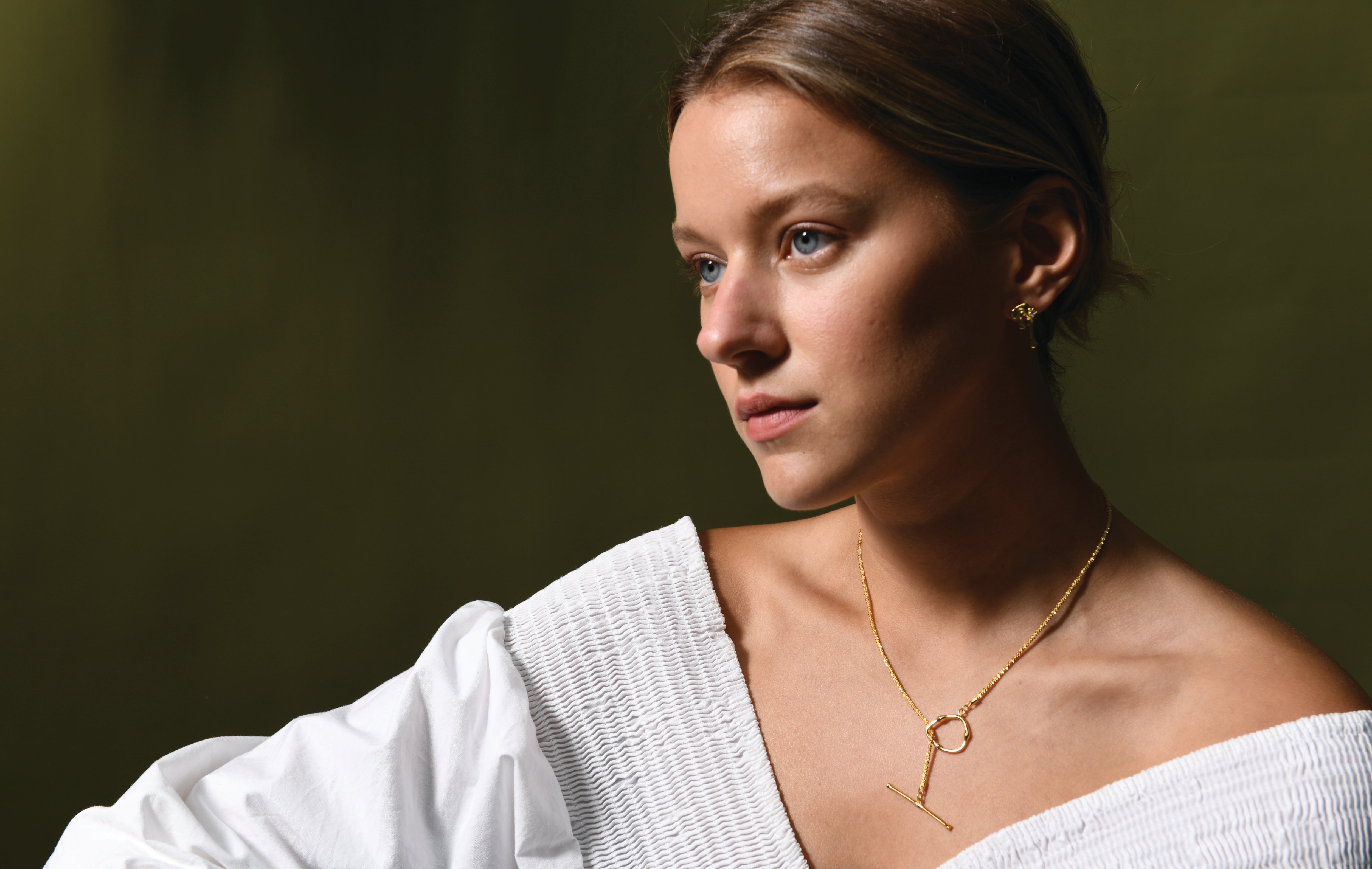 A female model wearing a gold plated necklace. The necklace has a dainty gold chain with a toggle clasp which can be worn at the front or back.