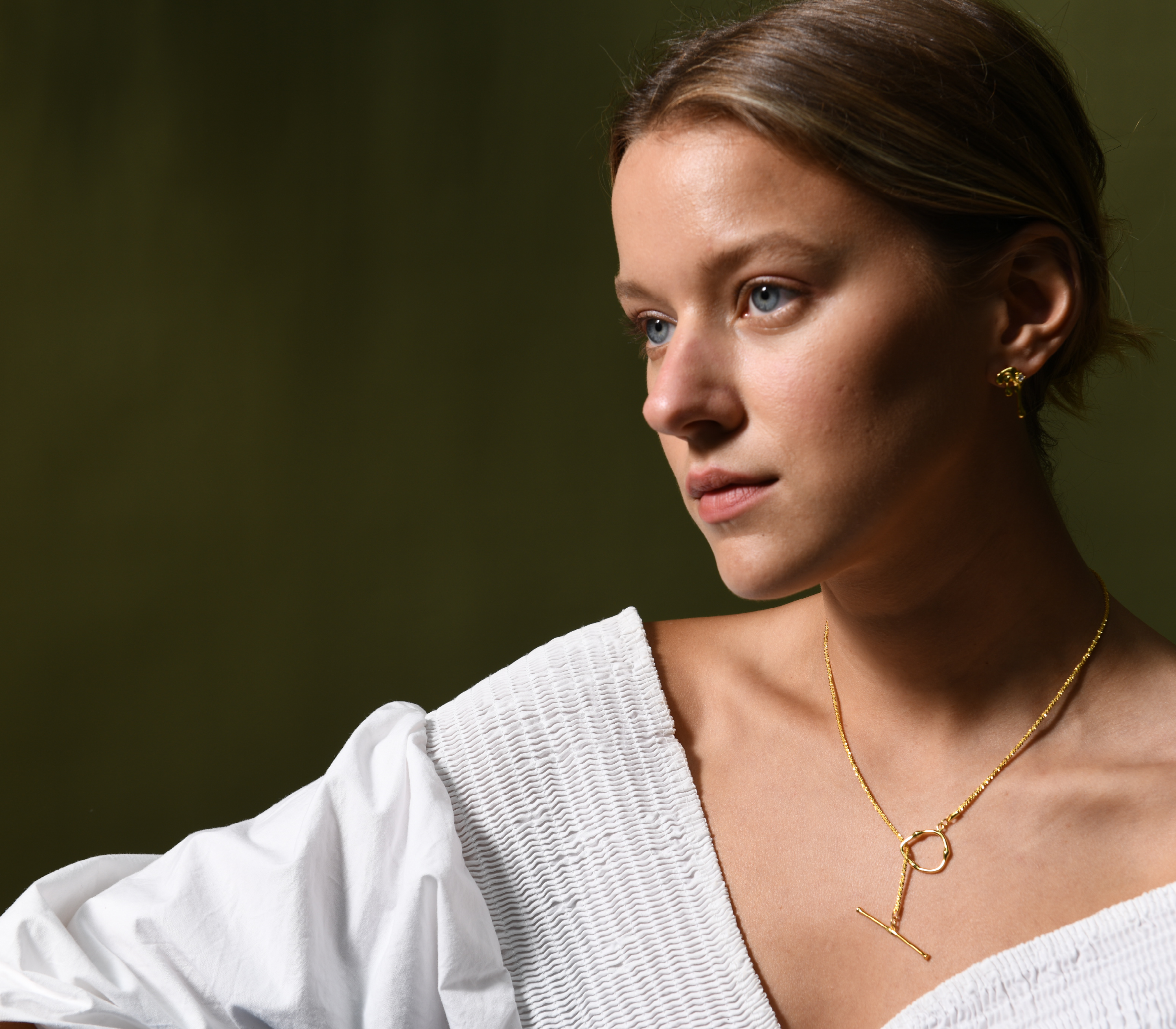 A female model wears a pair of gold vermeil earrings. She also wears a gold vermeil necklace with a dainty chain and toggle clasp.