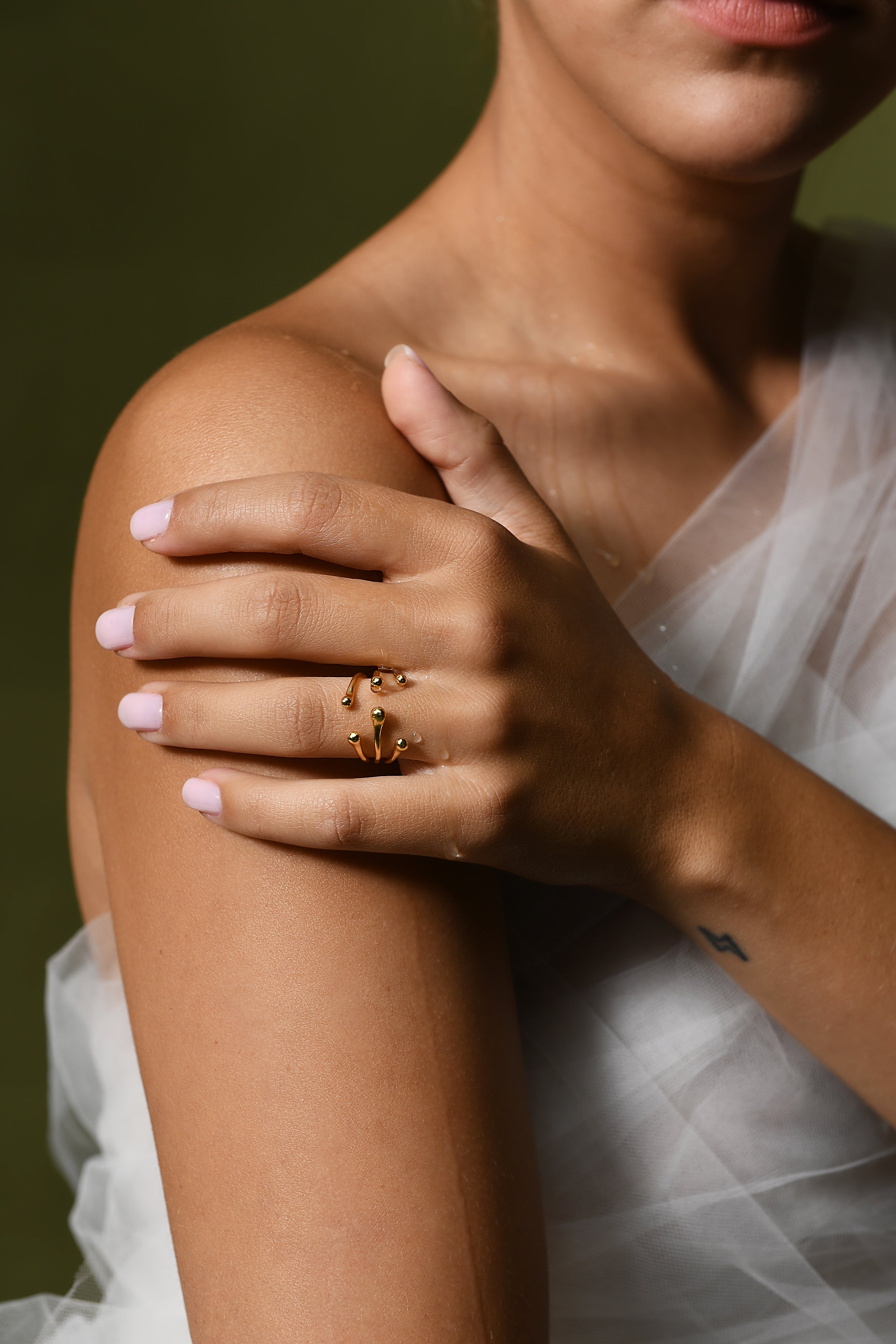 A female model poses with her hand on her shoulder, showing the open band gold ring she is wearing.