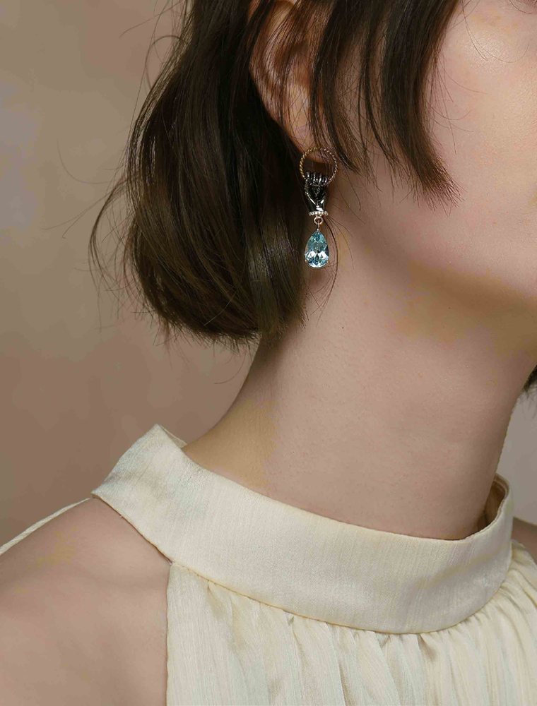 A model wearing a hoop stud earring with a fist holding onto the hoop. The earring also features a topaz gemstone.