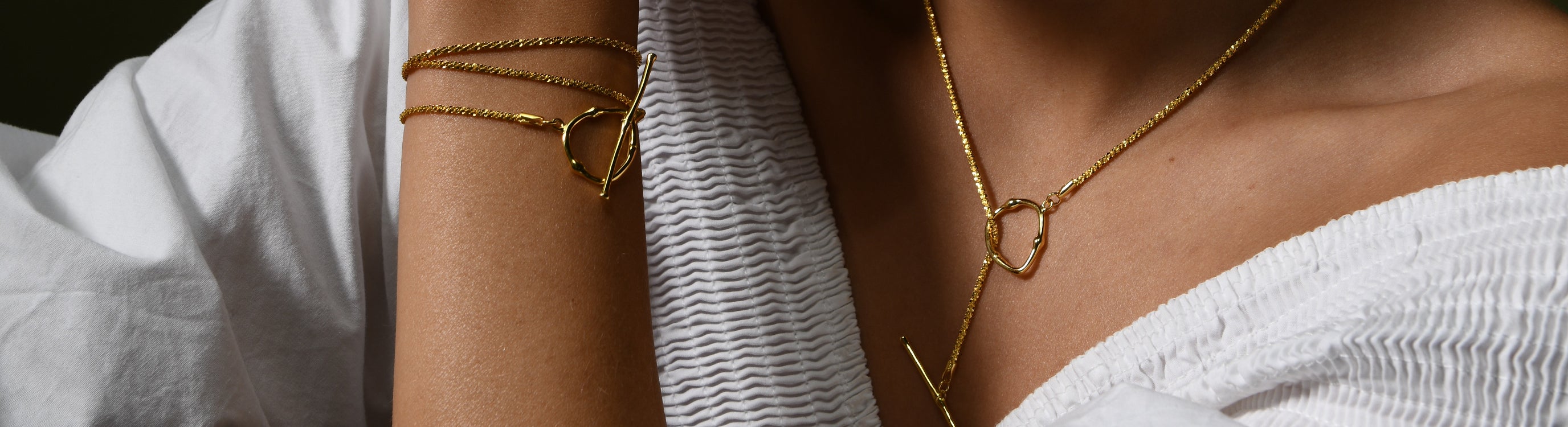 A female model wears a gold vermeil necklace with a dainty chain and toggle clasp. The model also wears a bracelet with a dainty chain and toggle clasp.