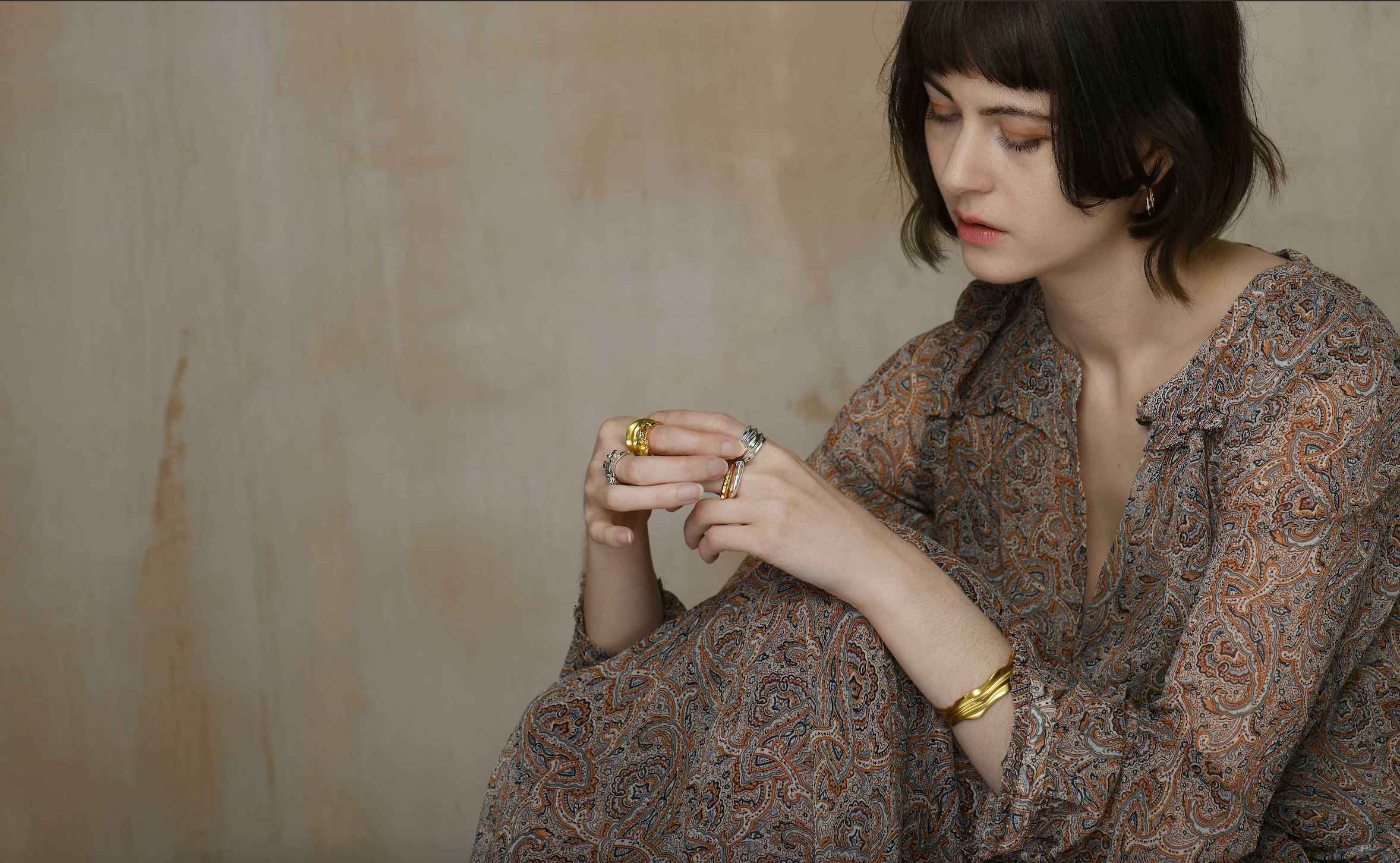A lady wearing a collection of both gold vermeil and sterling silver rings and a gold vermeil bangle. 
