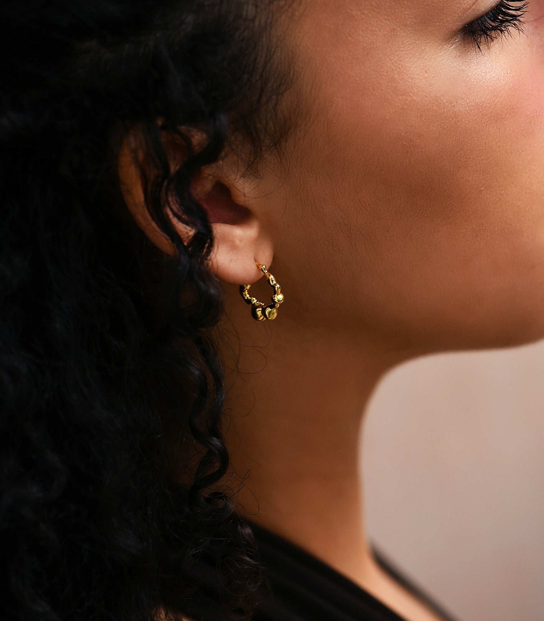 a pair of gold plated bubble shaped hoop earrings on a female model