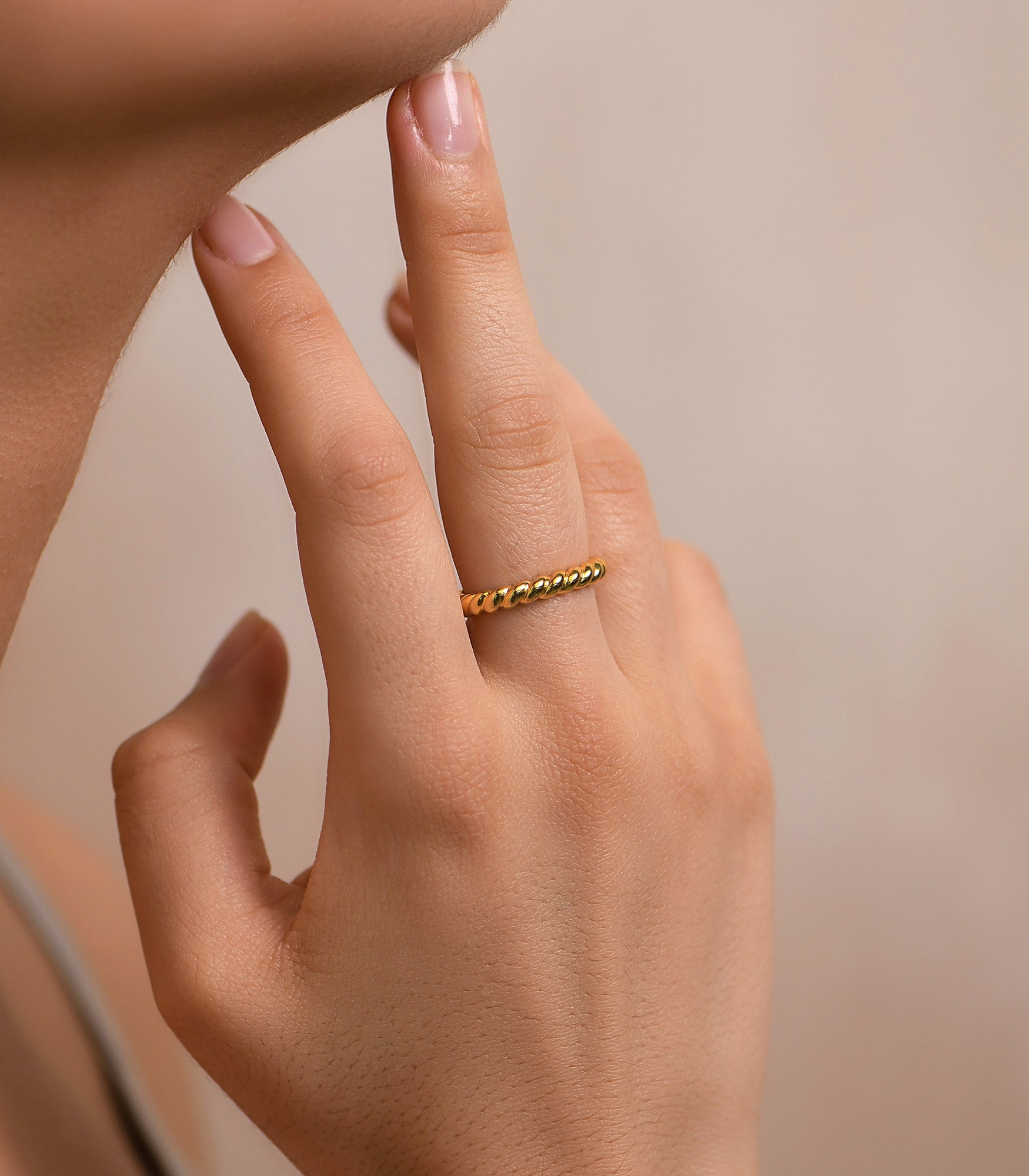 a close up of a female hand wearing a simple twist rope ring in gold. and polished finish