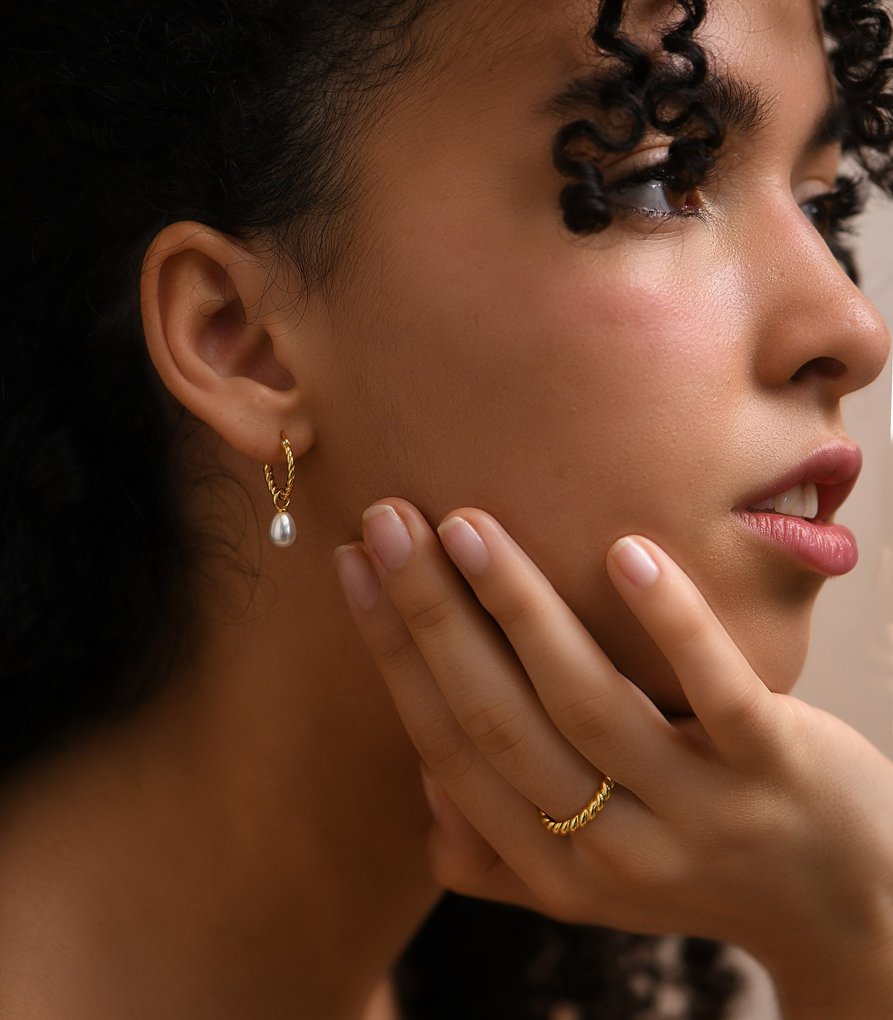 a pretty female model wearing a delicate twist rope huggie earrings with pearls and a matching twist rope ring band on her midfinger