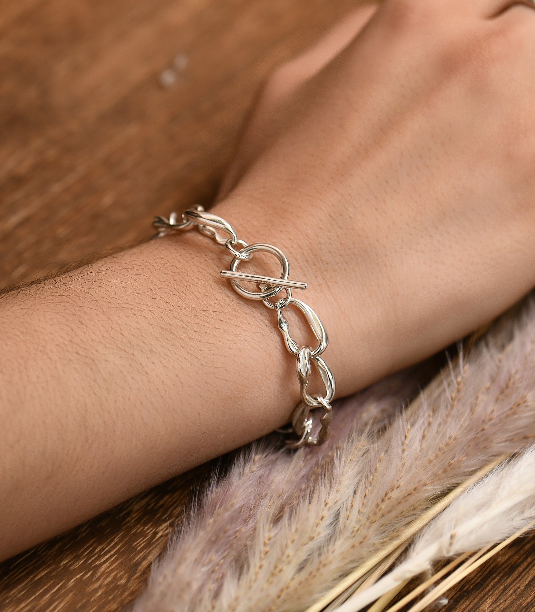 a female hand wearing a irregular oval shaped silver link bracelet, toggle clasp