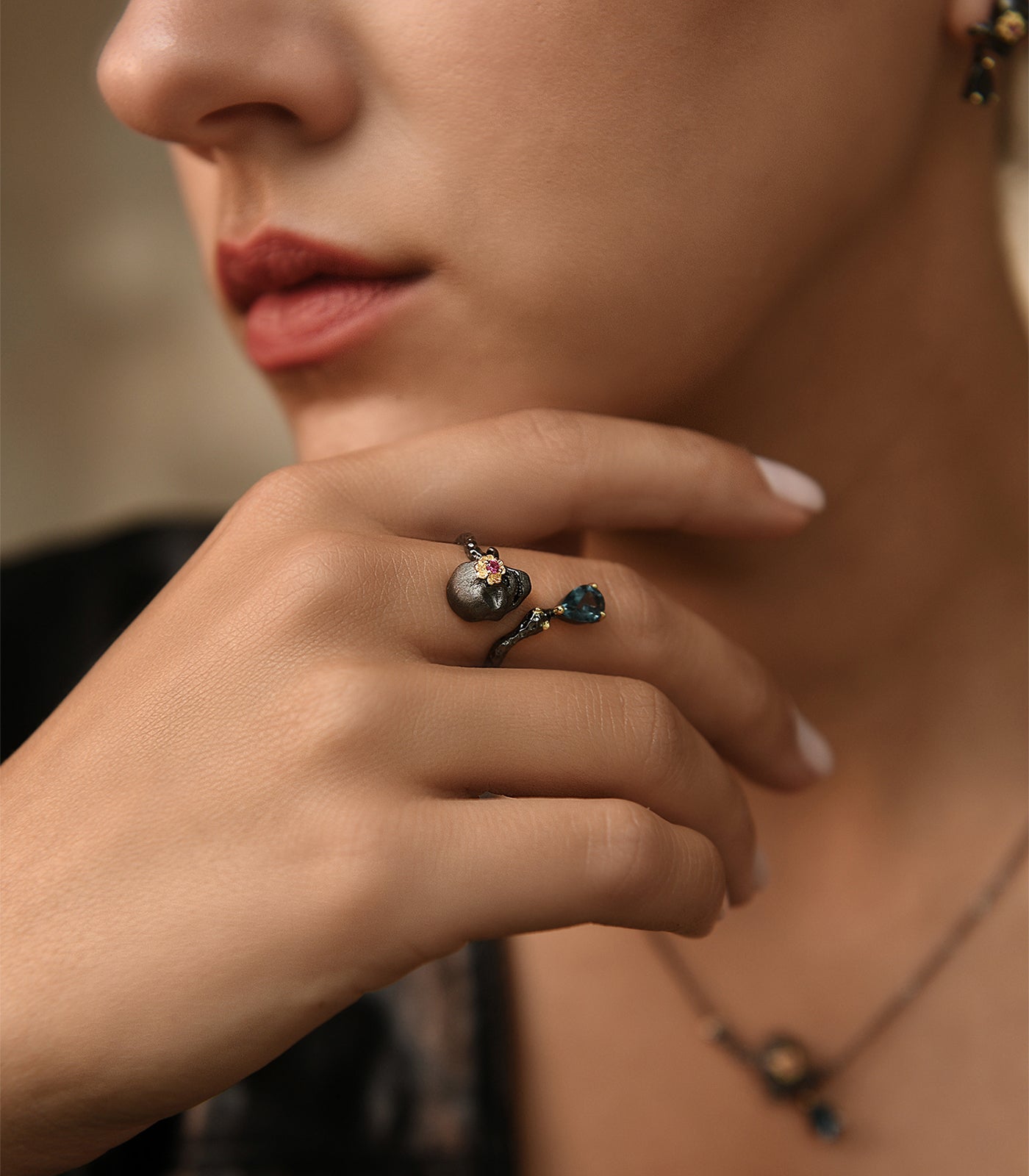 An oxidised sterling silver ring with an open band design featuring a skull with a pink ruby and blue topaz gemstone.