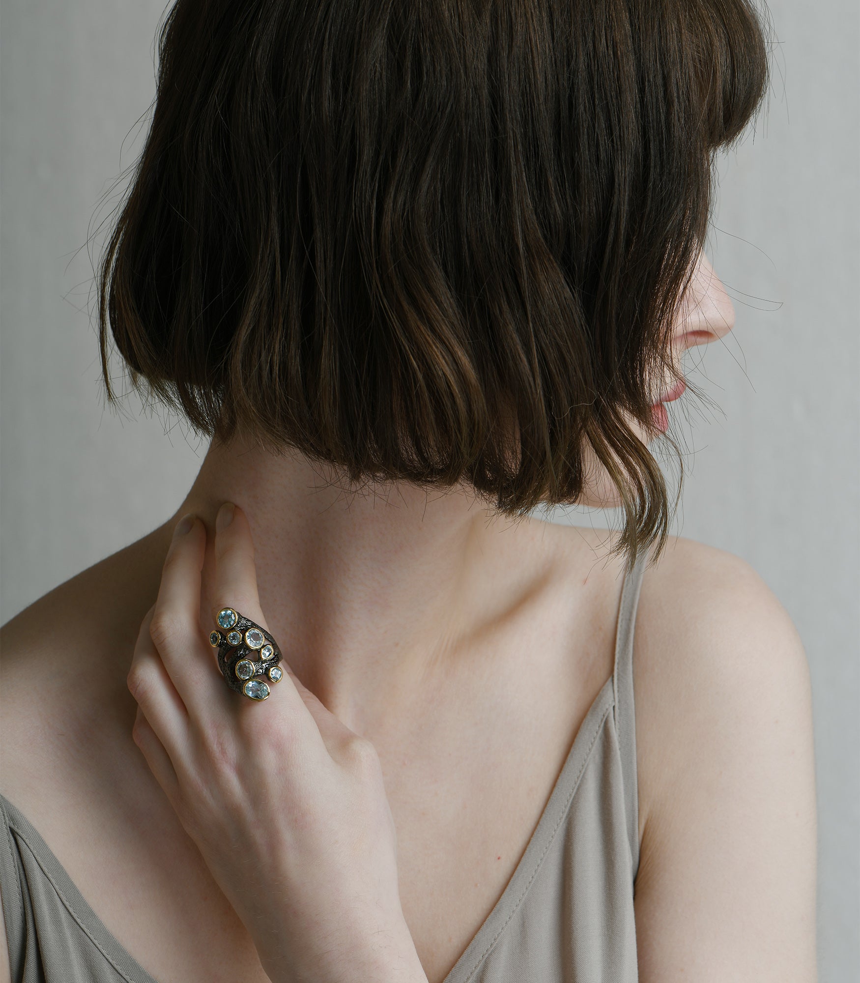 A model wearing an oxidised sterling silver eyelet ring. The ring has an irregular shape with 8 blue topaz stones.