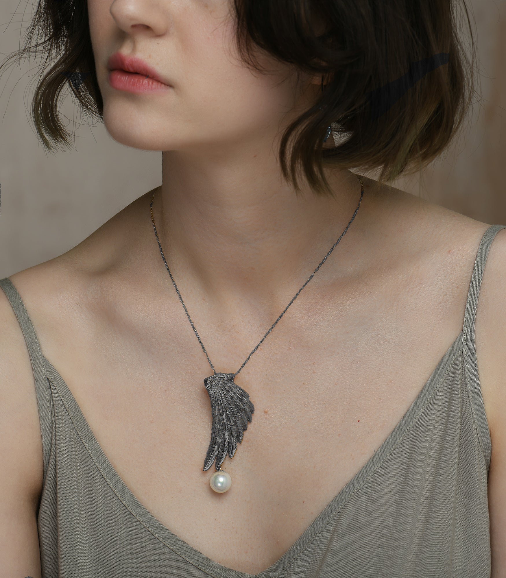 A lady wearing a sterling silver necklace with an eagle wing pendant which has a white pearl hanging from it.