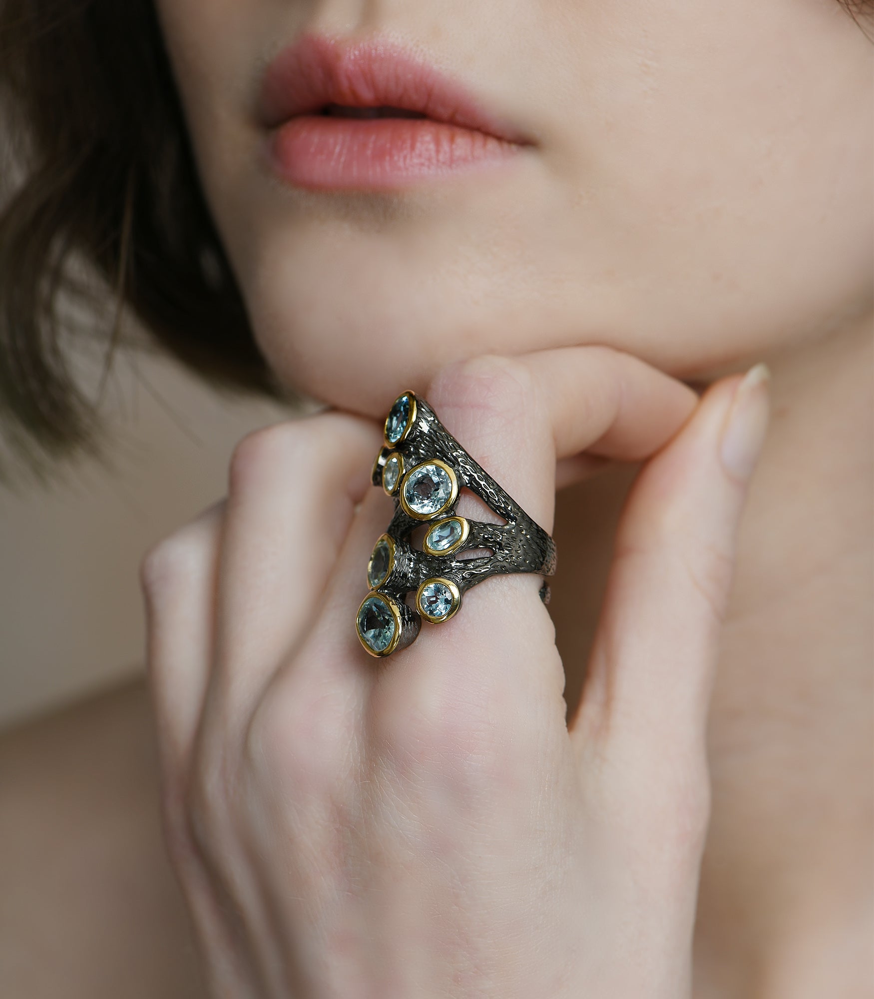 An oxidised sterling silver ring. The ring has an irregular shape with gold detailing and 8 blue topaz stones.