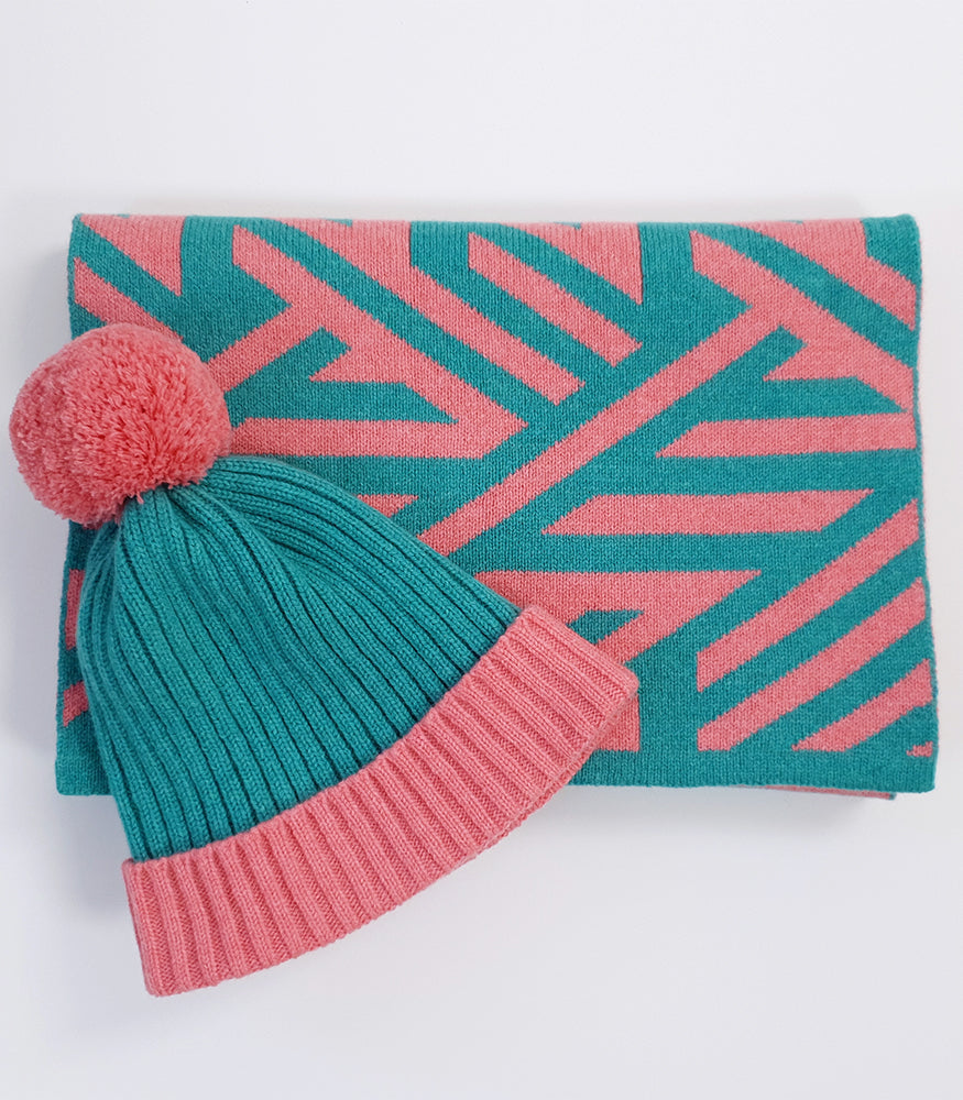 A pink and blue bobble hat with a matching scarf. The scarf has a geometric crosswise pattern.