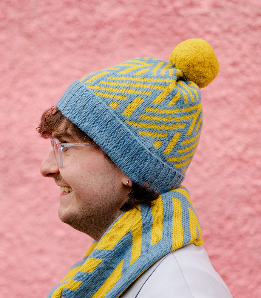 A man wearing a knitted, blue and yellow crosswise patterned hat and matching scarf.