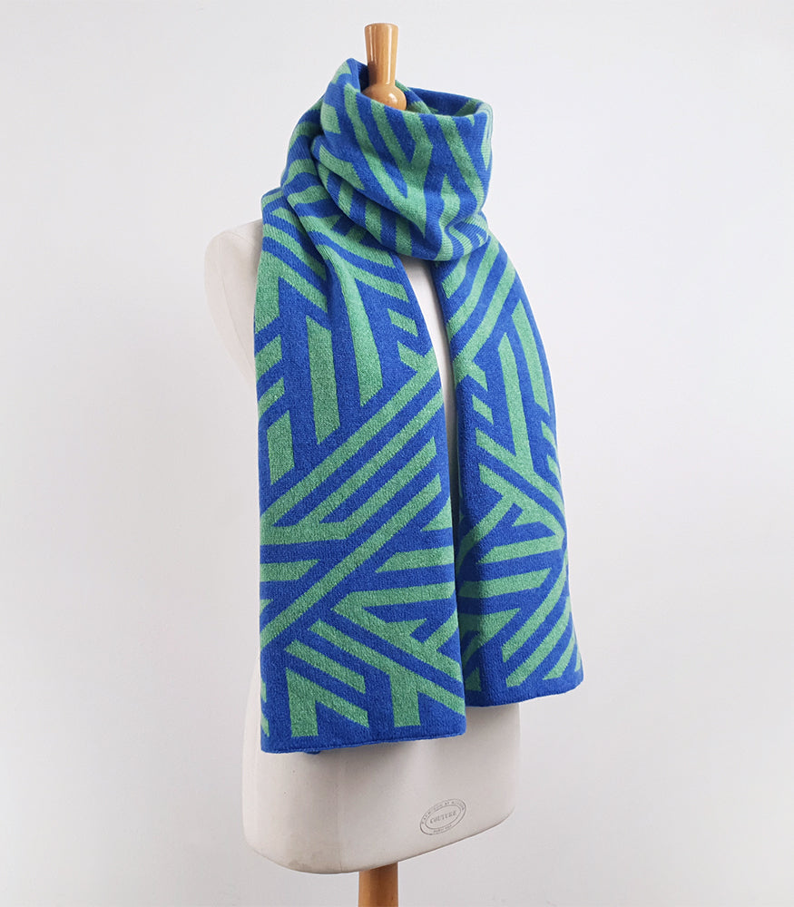A long and wide knitted lambswool scarf. The scarf has a geometric crosswise blue and green pattern.