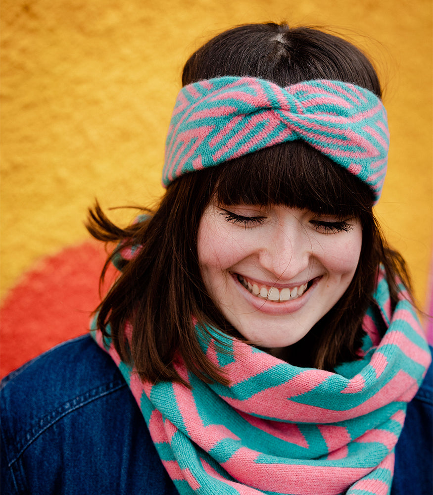 A lady wearing a pink and blue crosswise pattern twist headband and matching snood. 