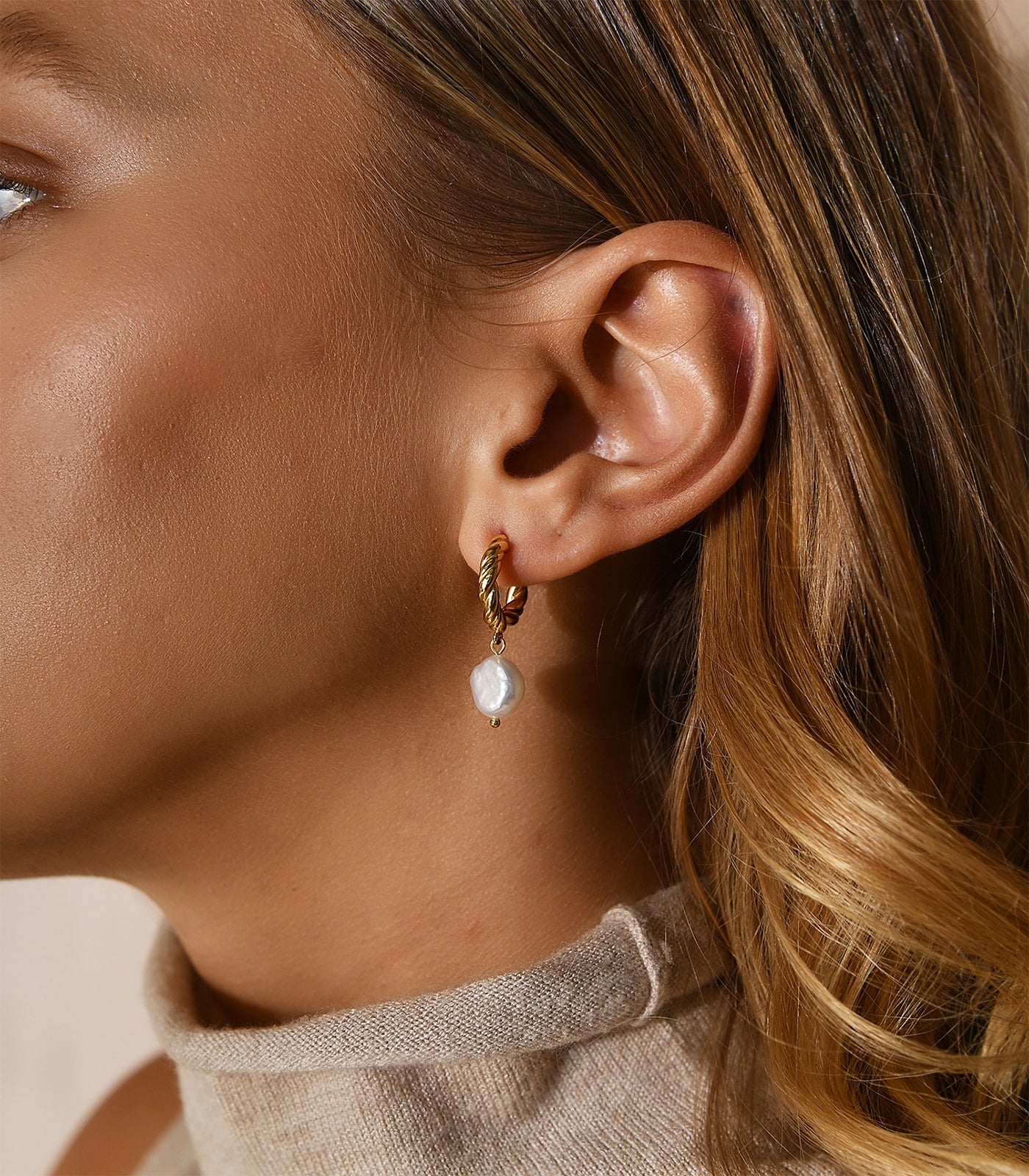 A gold vermeil small twisting hoop earring with a baroque pearl hanging from the hoop.