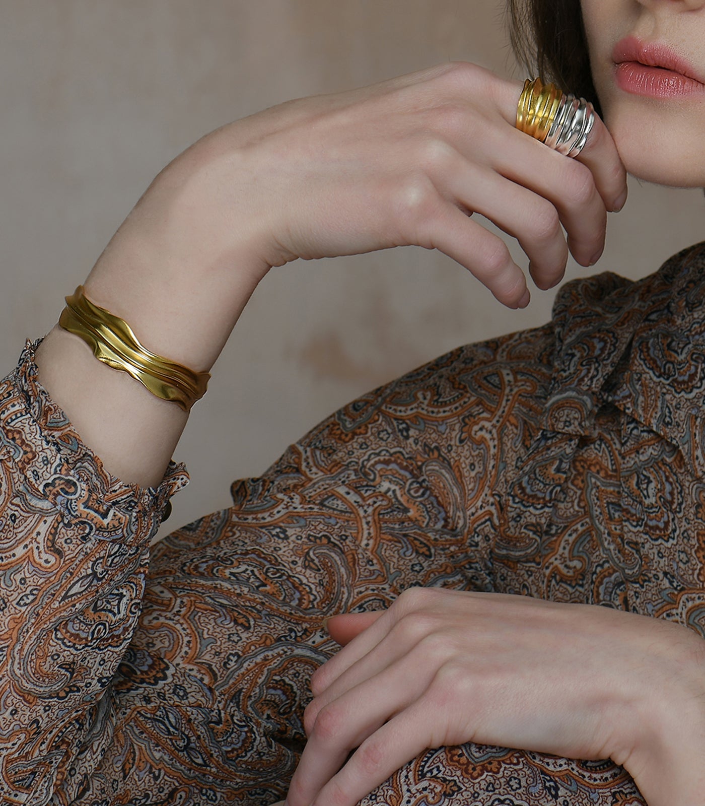 A model wears a gold vermeil bangle and ring with a sterling silver ring. All 3 pieces feature similar smooth valleys and ridges.