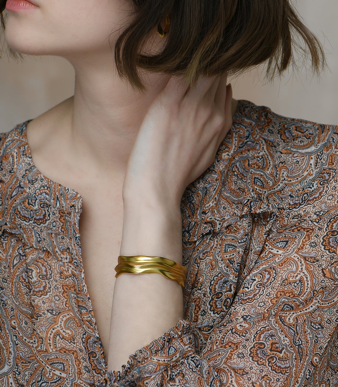 A gold vermeil bangle being worn by a model. The bangle has an organic shape, reflecting the texture of sandunes.