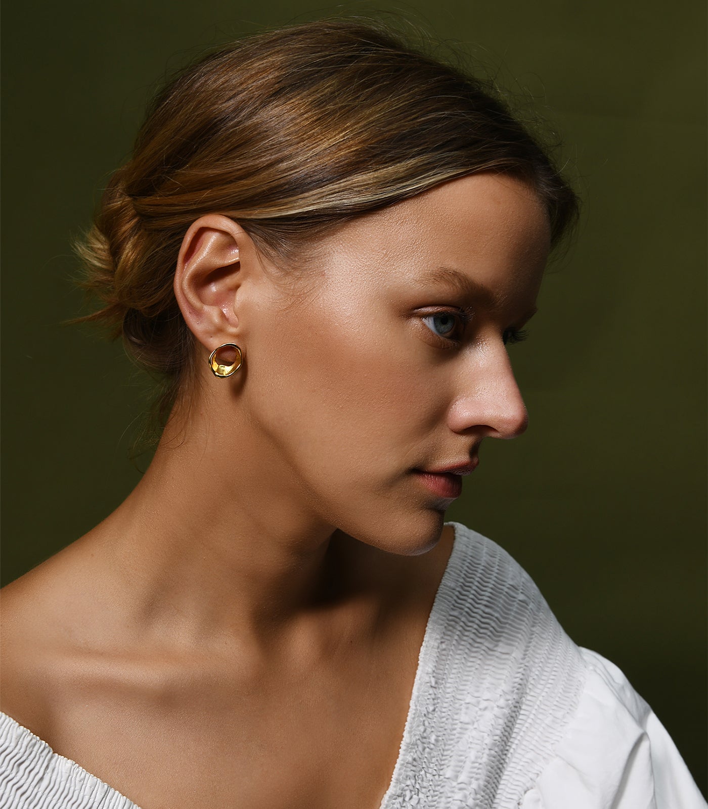 A model wears a gold vermeil circle stud earring. The earring has an organic shape similar to the movement of flowing water.