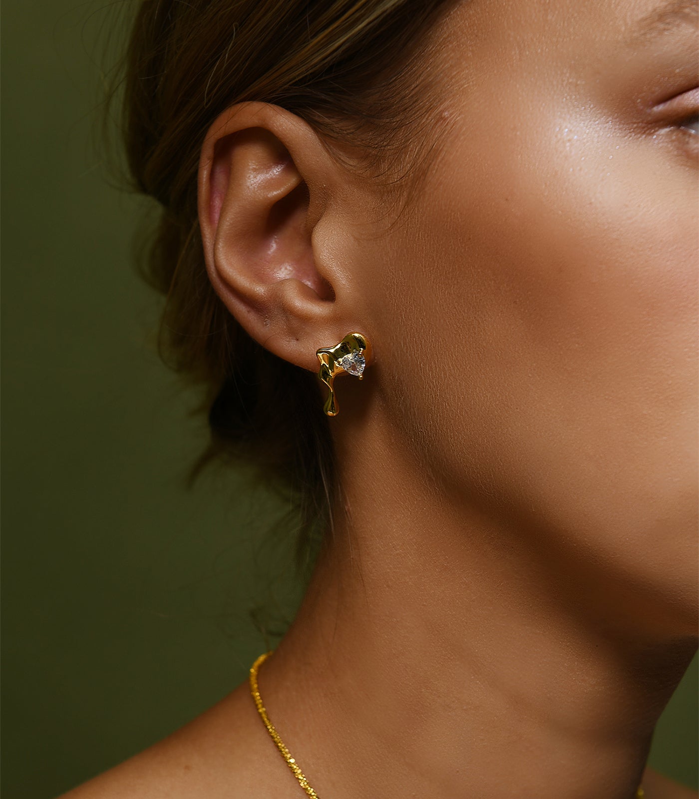 A model wears a pair of gold vermeil, stud earrings which resemble a droplet of water.