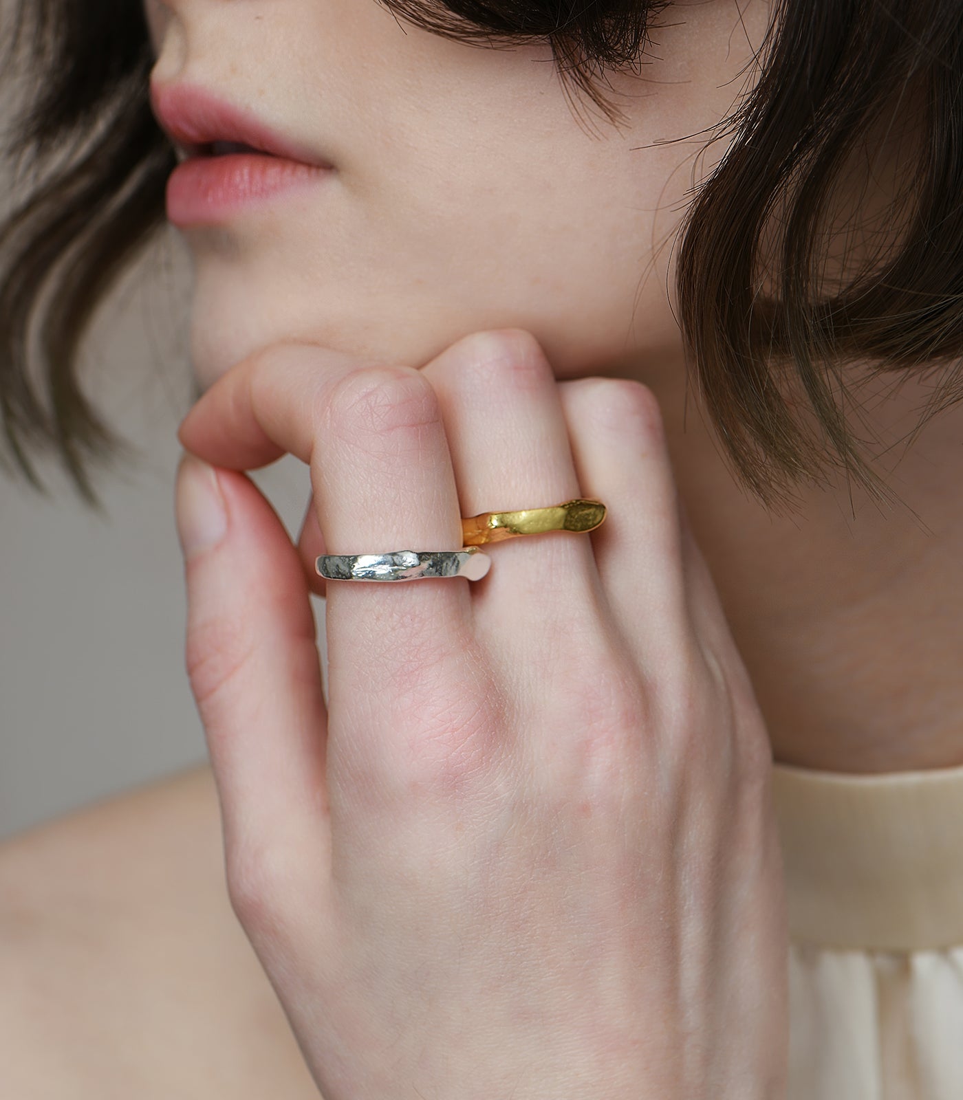 A model wears two silver and gold rings. The rings have a chunky band and organic rocky texture.
