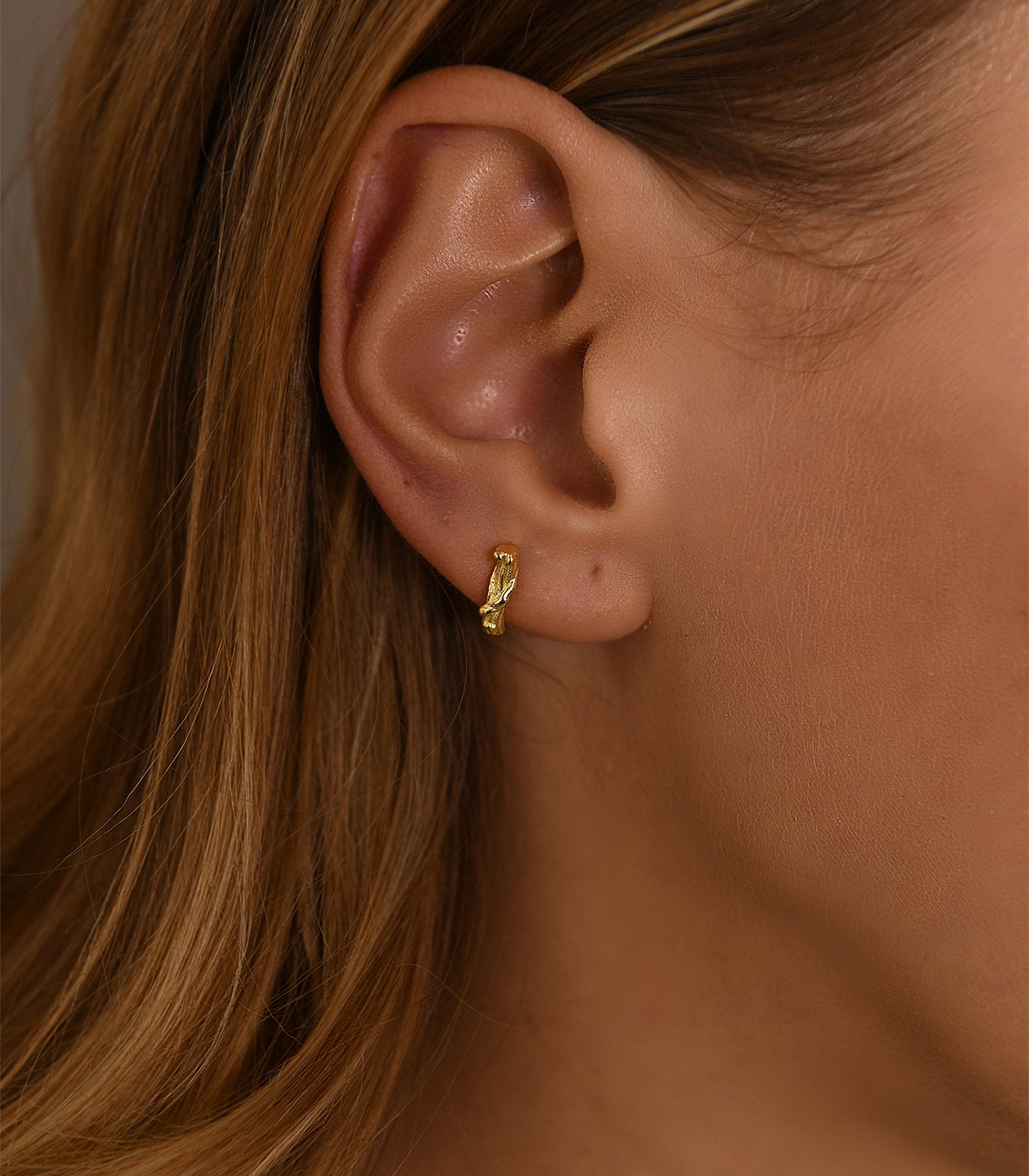 A gold vermeil stud earring. The stud earring is detailed to resemble a tree branch.