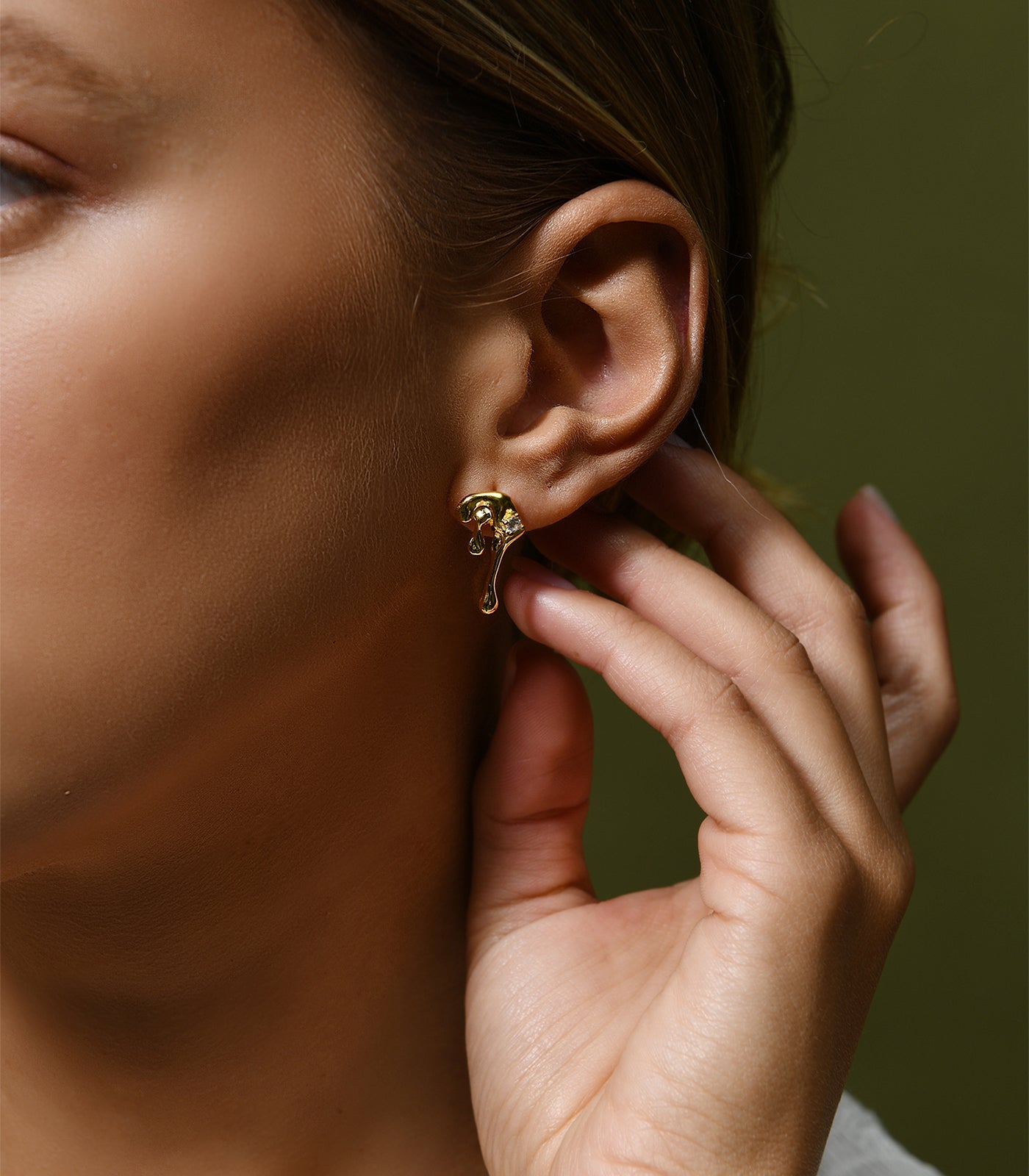 A model wears a pair of gold vermeil stud earrings, shaped to resemble water droplets.