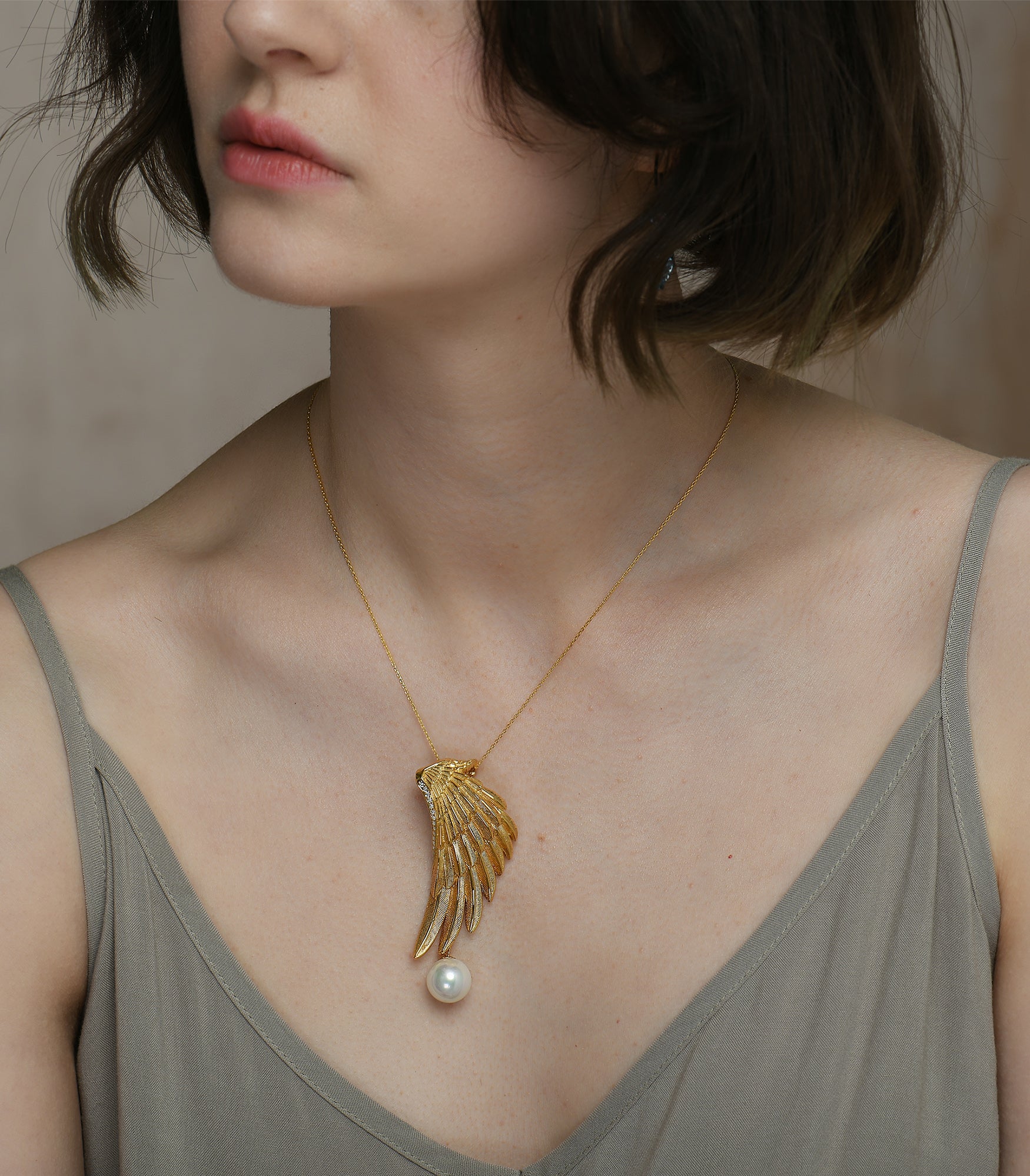 A lady wearing a gold vermeil necklace which has an eagle wing pendant  with a white pearl hanging from it.