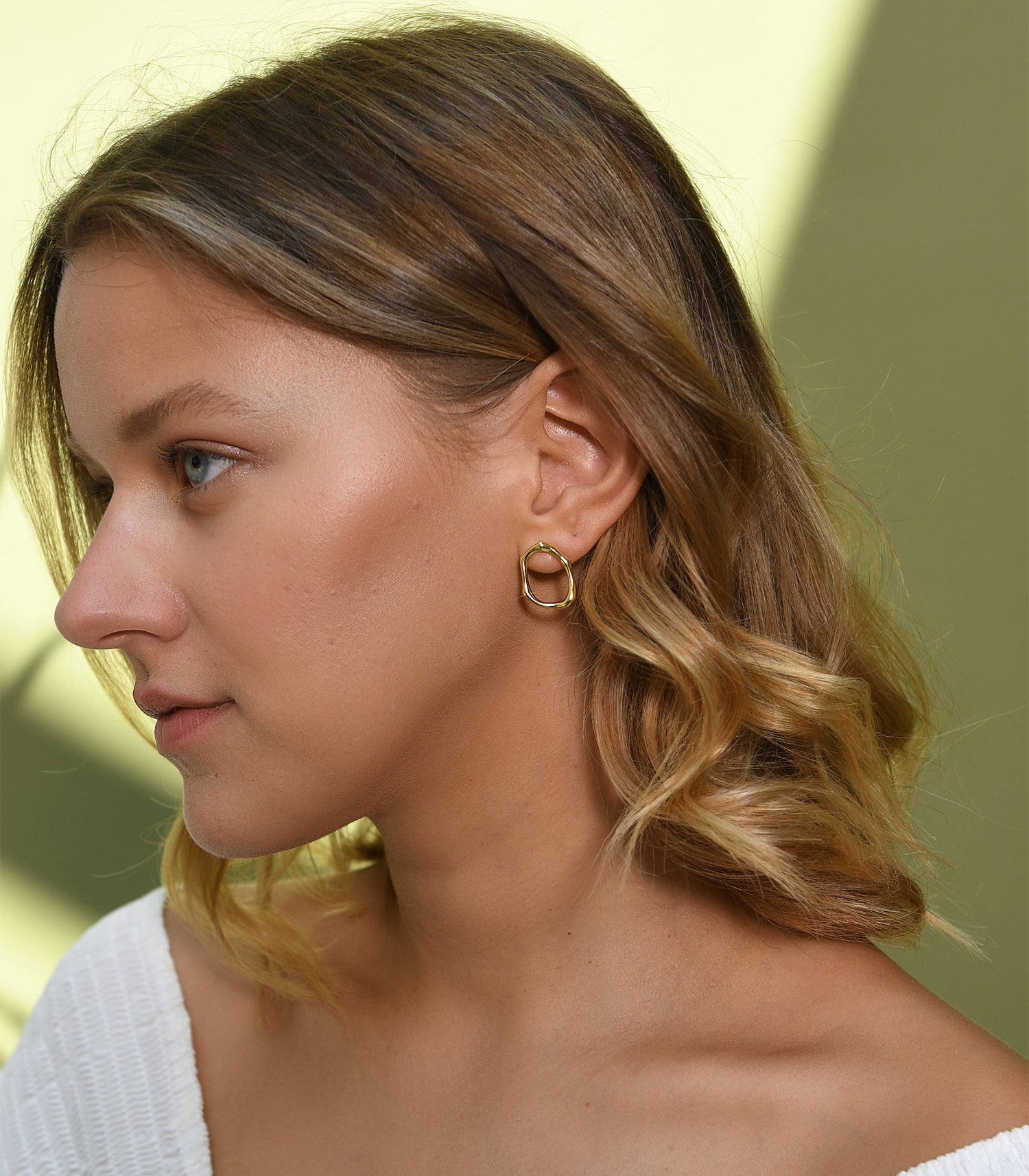 A model wearing a gold vermeil, circle stud earring. The circle has an irregular shape.