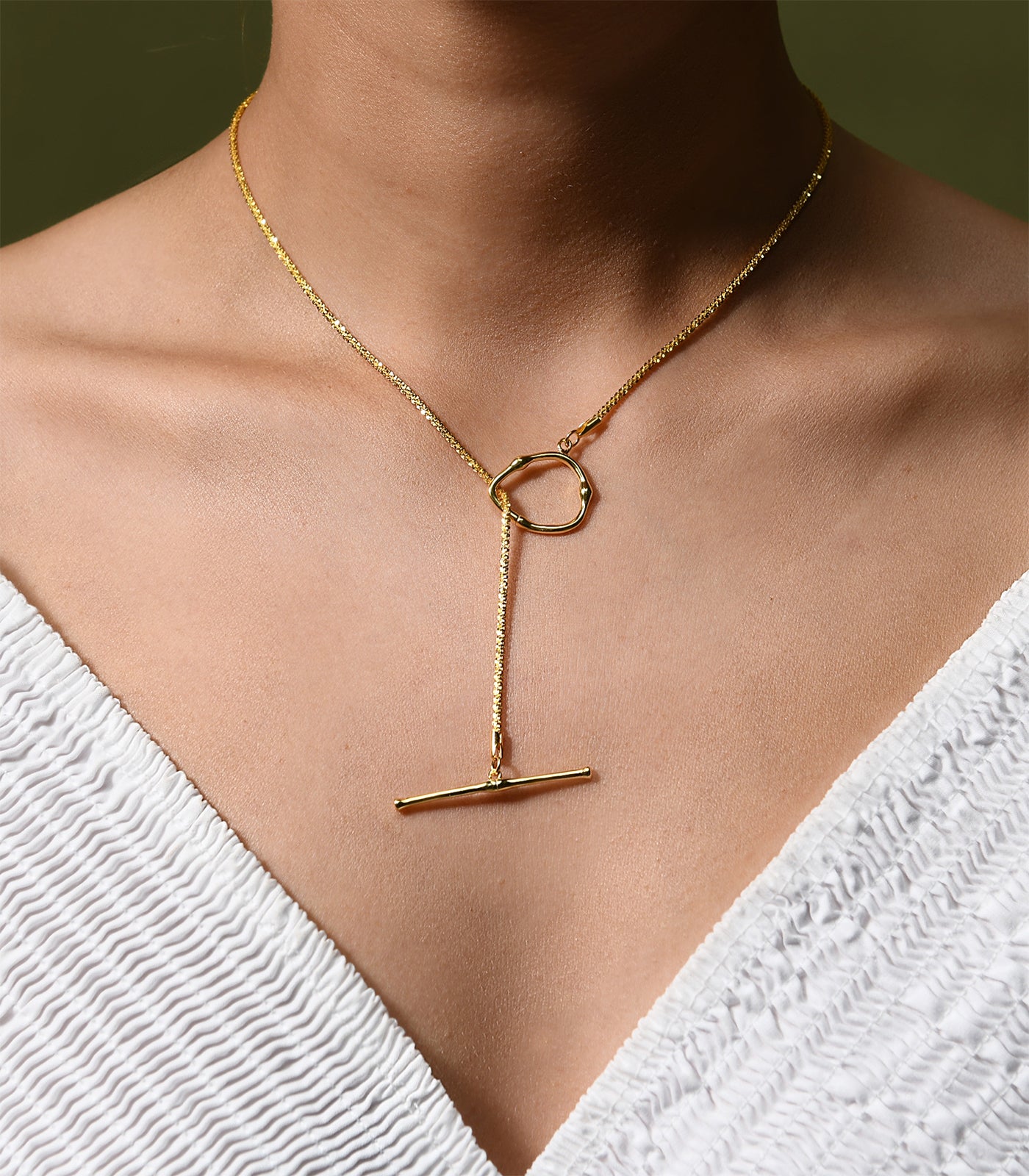 A  gold vermeil necklace which has a dainty chain and a toggle clasp design worn at the front.