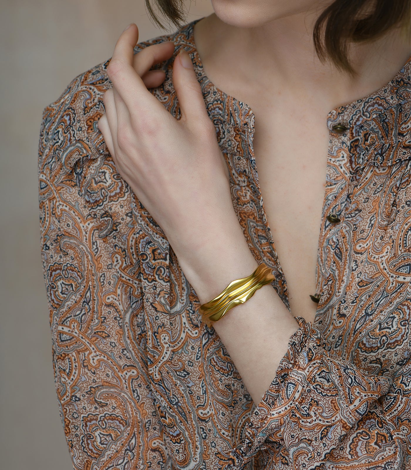 A gold vermeil bangle being worn by a model. The bangle has an organic shape with valleys, reflecting the shape of sandunes.