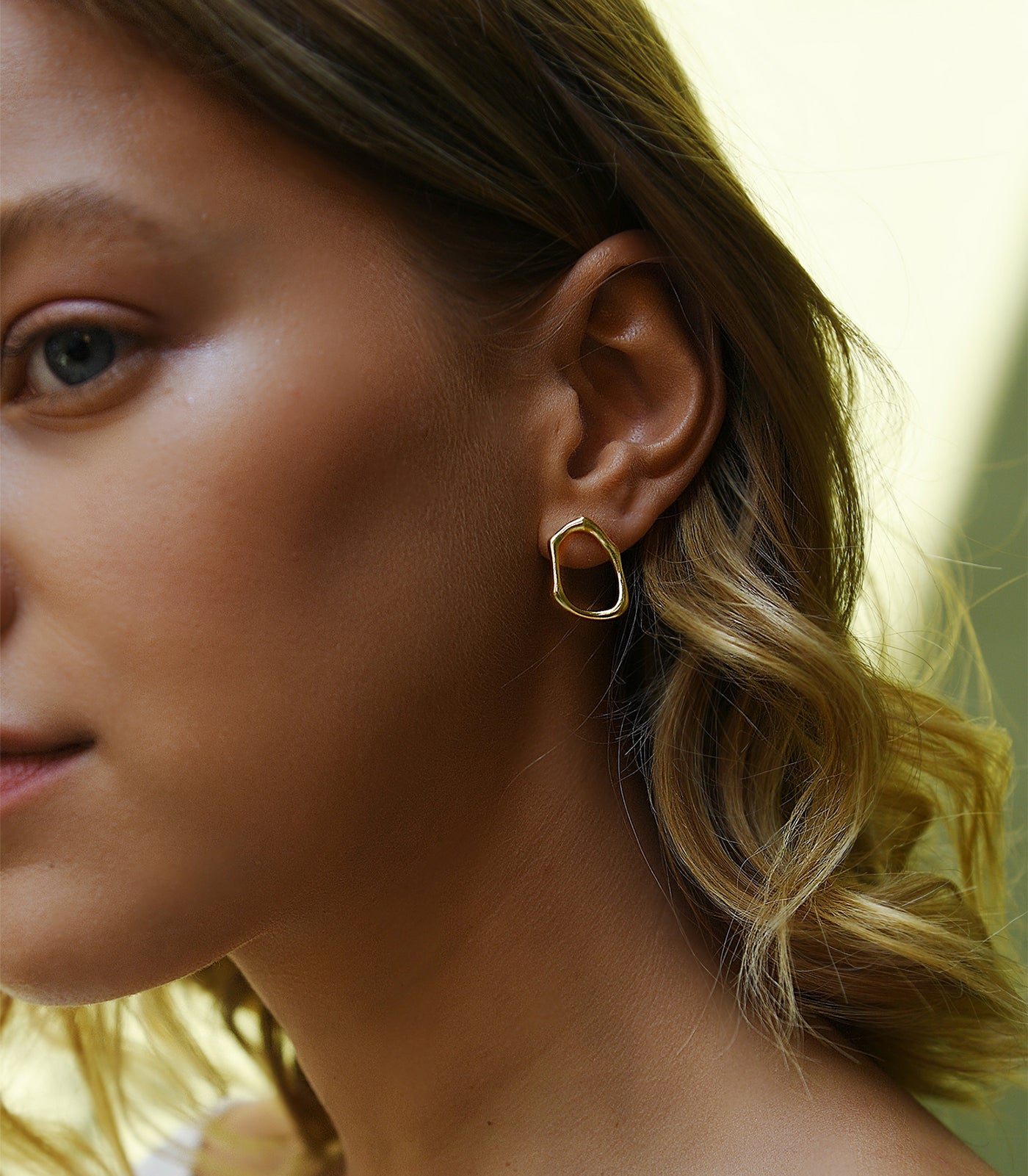 A model wears a gold vermeil, irregularly shaped, circle stud earring.