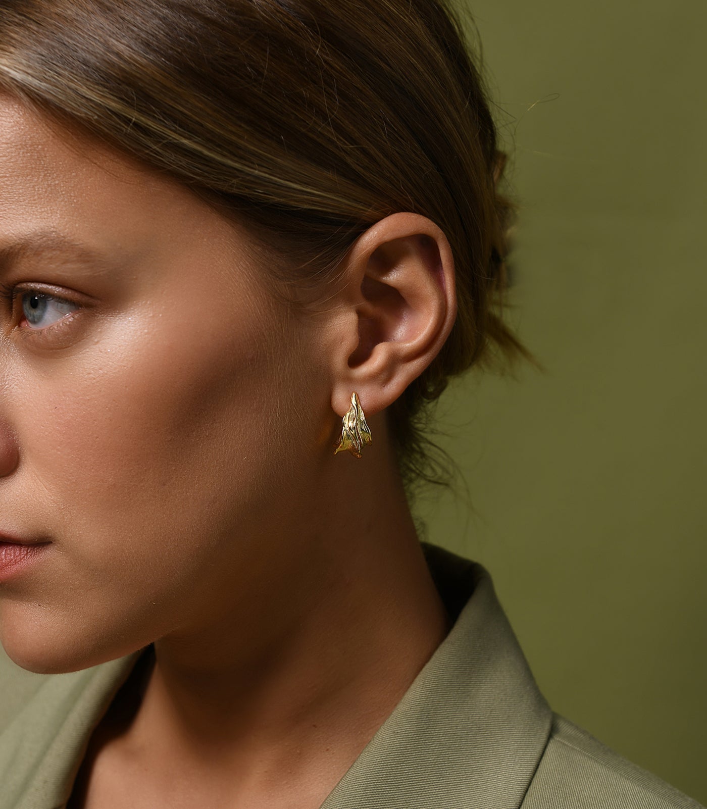 A model wears a pair of gold vermeil, large leaf, textured hoop earrings.