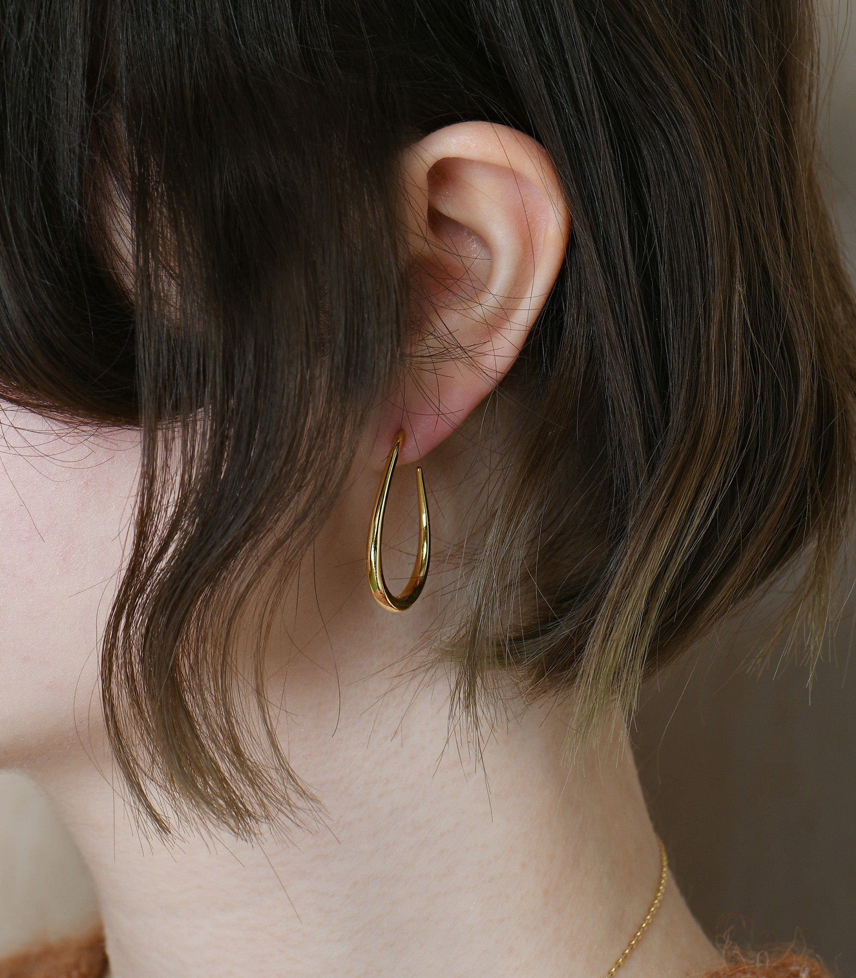 A pair of gold vermeil polished earrings on a model. The earrings are an oval teardrop shape.