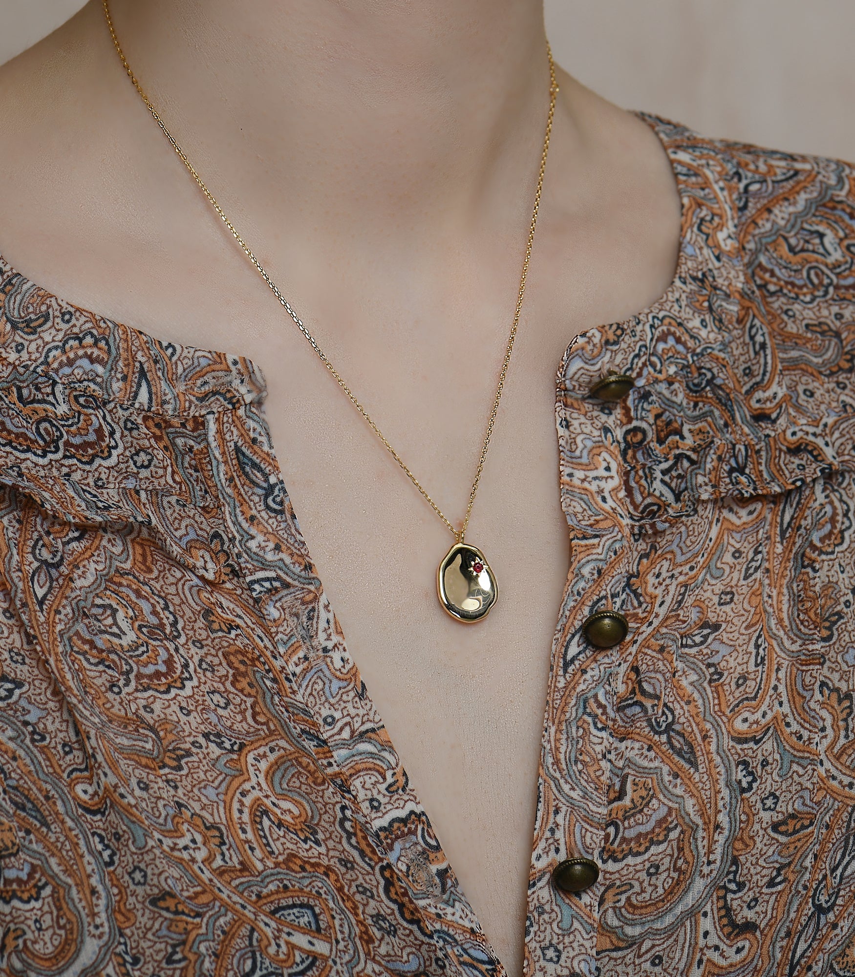A model wears a gold vermeil necklace with a pebble pendant featuring a ruby stone.
