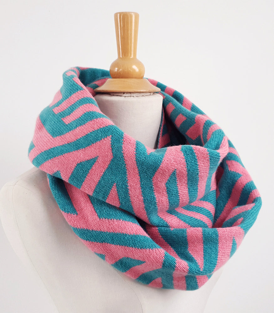 A pink and blue knitted lambswool snood. The snood has a geometric crosswise pattern.