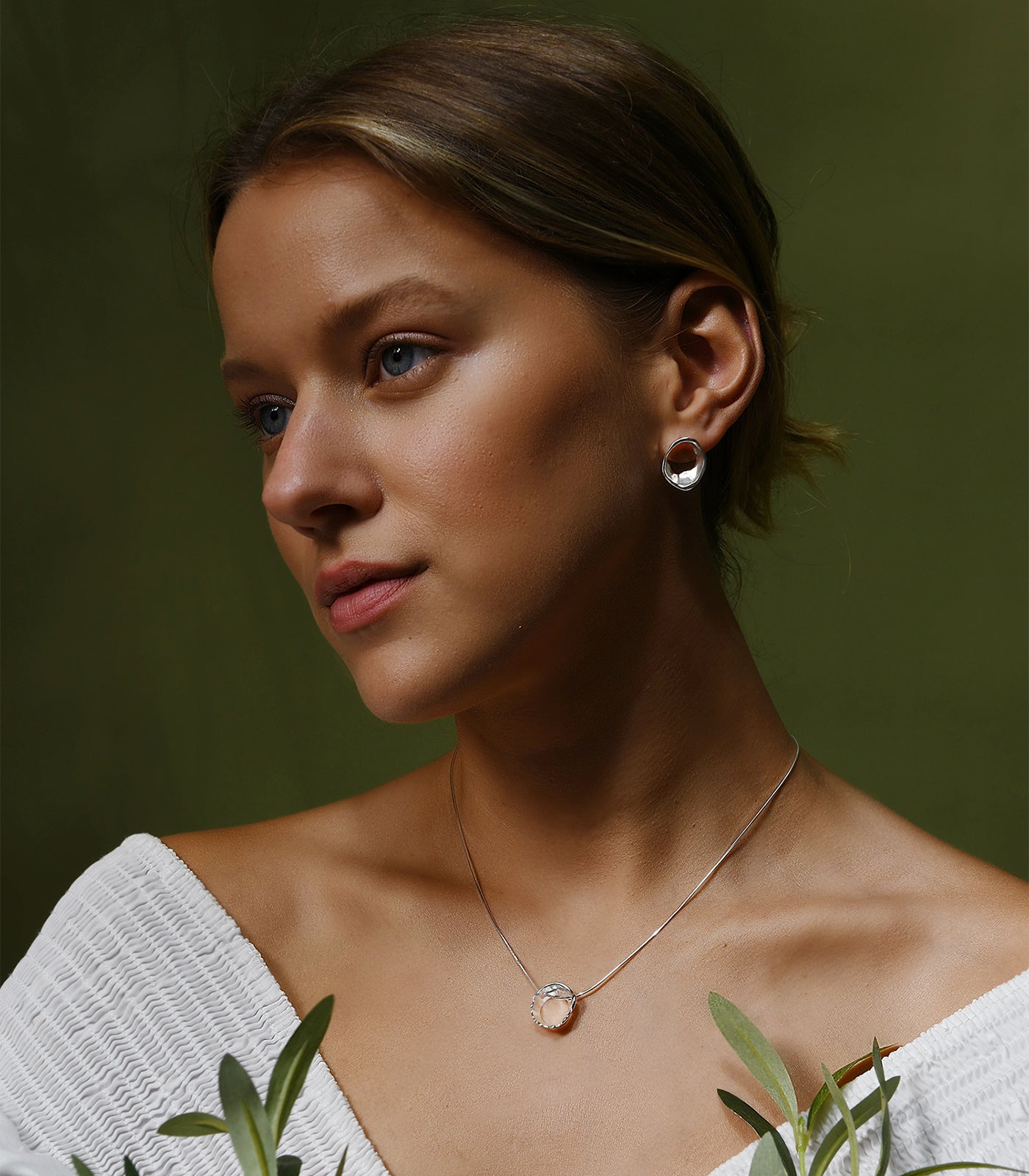 A model wears a pair of sterling silver circle stud earrings. The earrings have an irregular shape resembling waters movement.