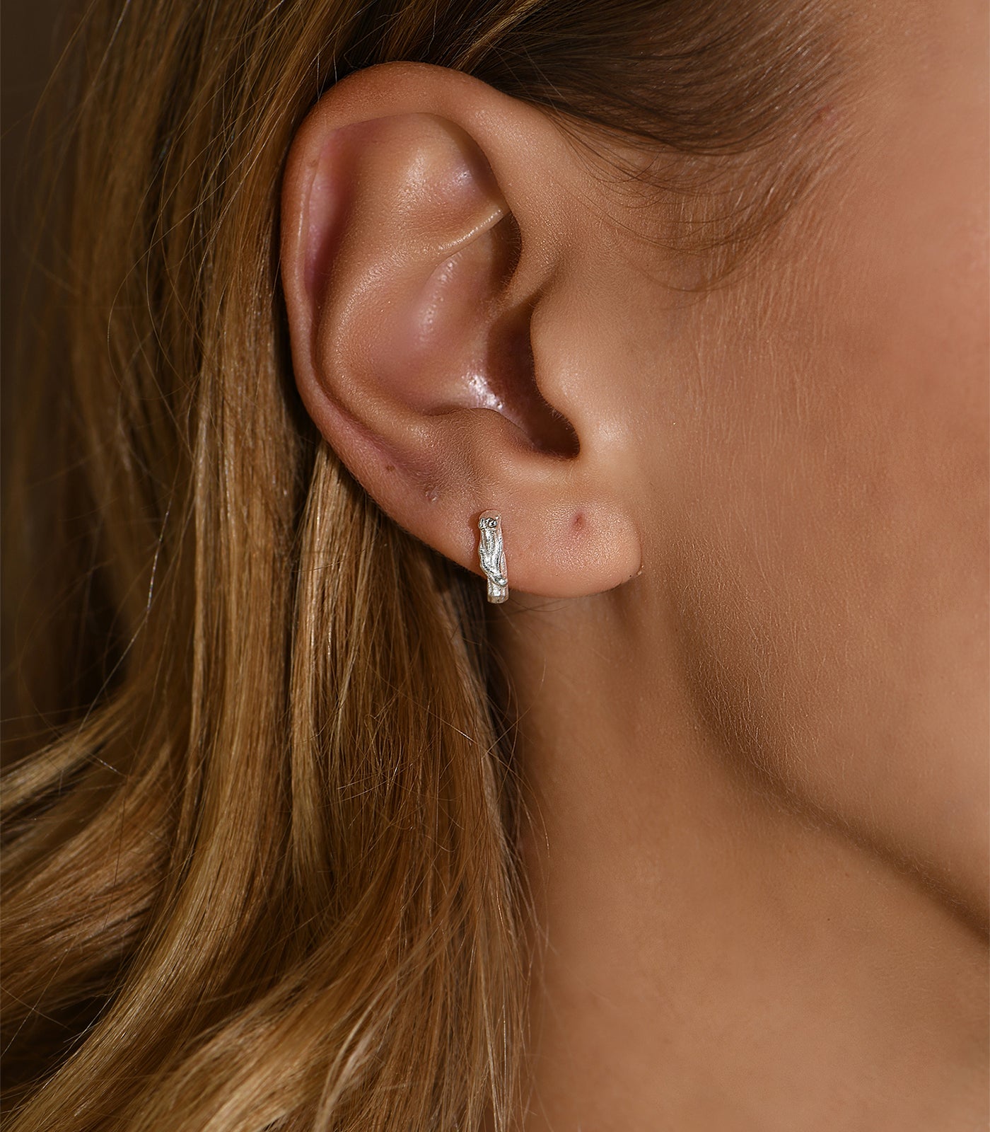 A sterling silver stud earring. The earring is detailed to resemble a small tree branch.