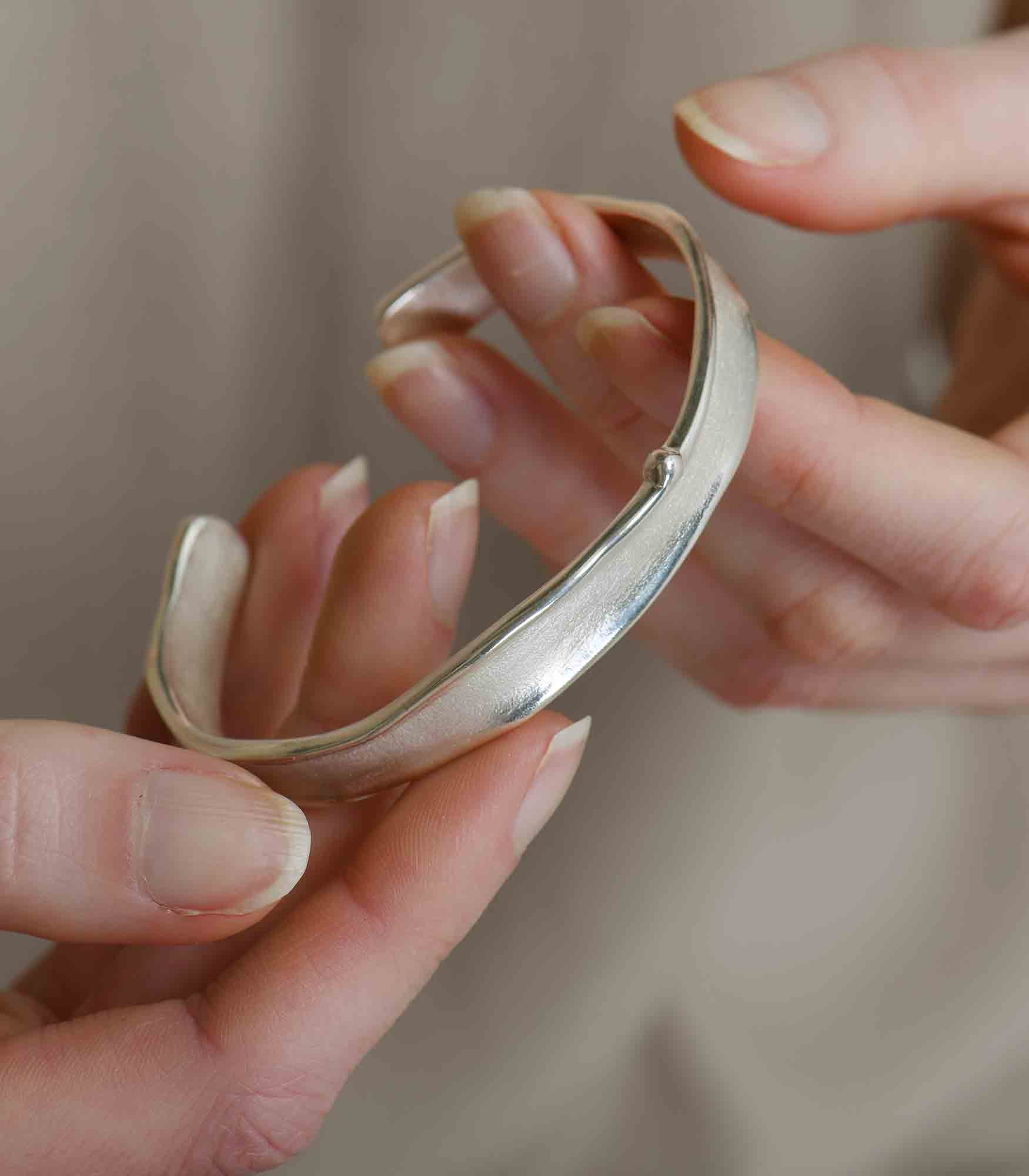 A sterling silver bangle bracelet featuring a minimalistic design with a simple brushstroke texture.