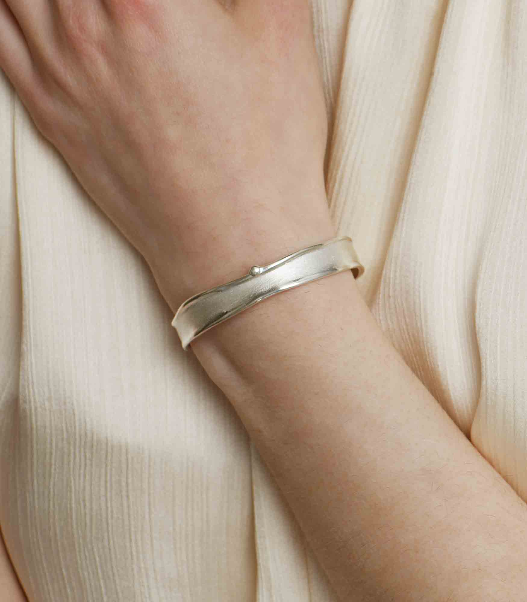 A sterling silver bangle bracelet which features a minimalistic design and a simple brushstroke texture.